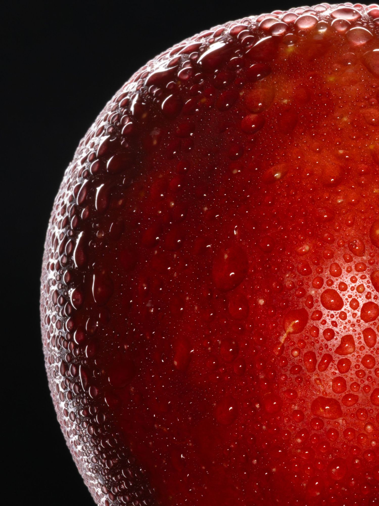 Close-up macro shot of red apple surface covered in water droplets against dark background.