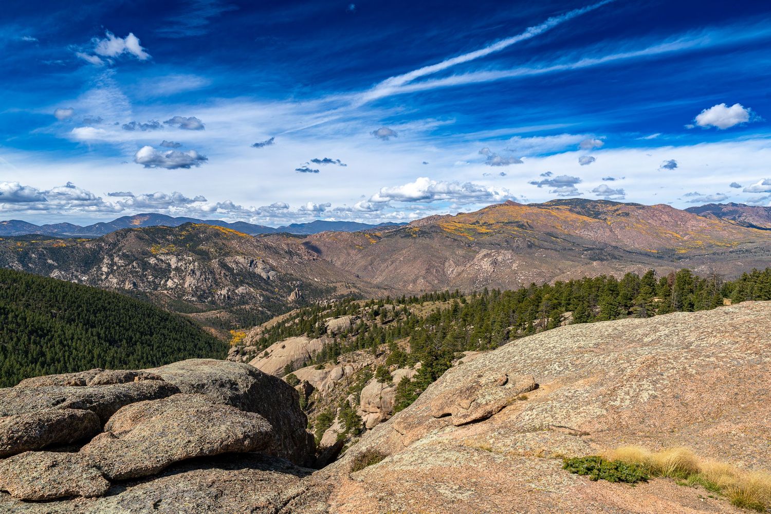 Rocky mountain terrain with expansive views of forested peaks under bright blue skies.