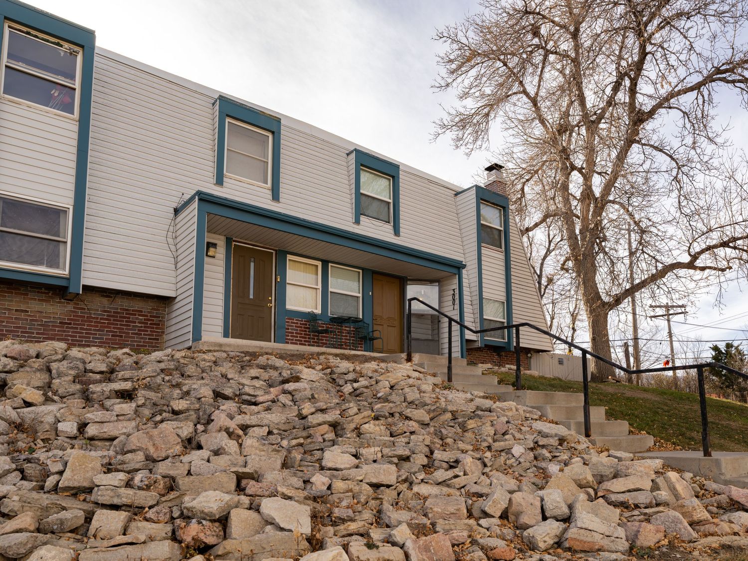 Exterior view of townhomes with stone retaining wall and bare trees in winter.