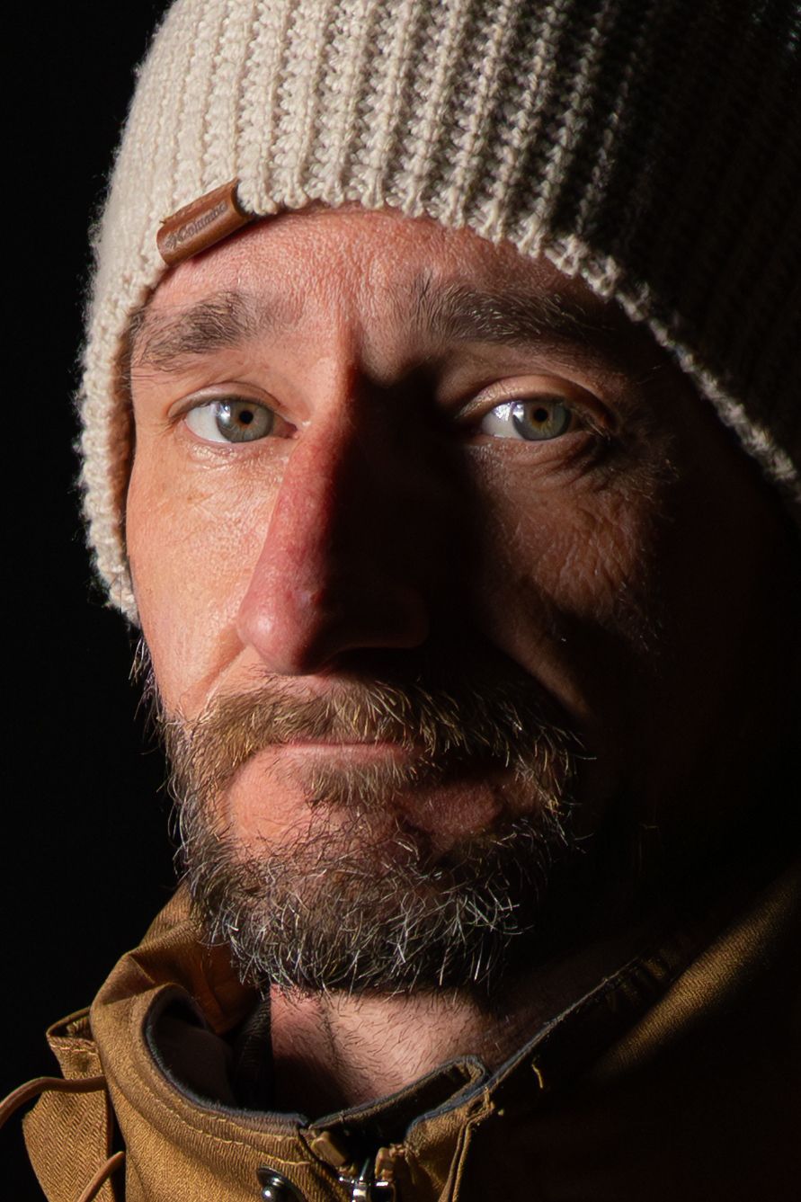 Close-up portrait of person wearing cream knit beanie against dark background.