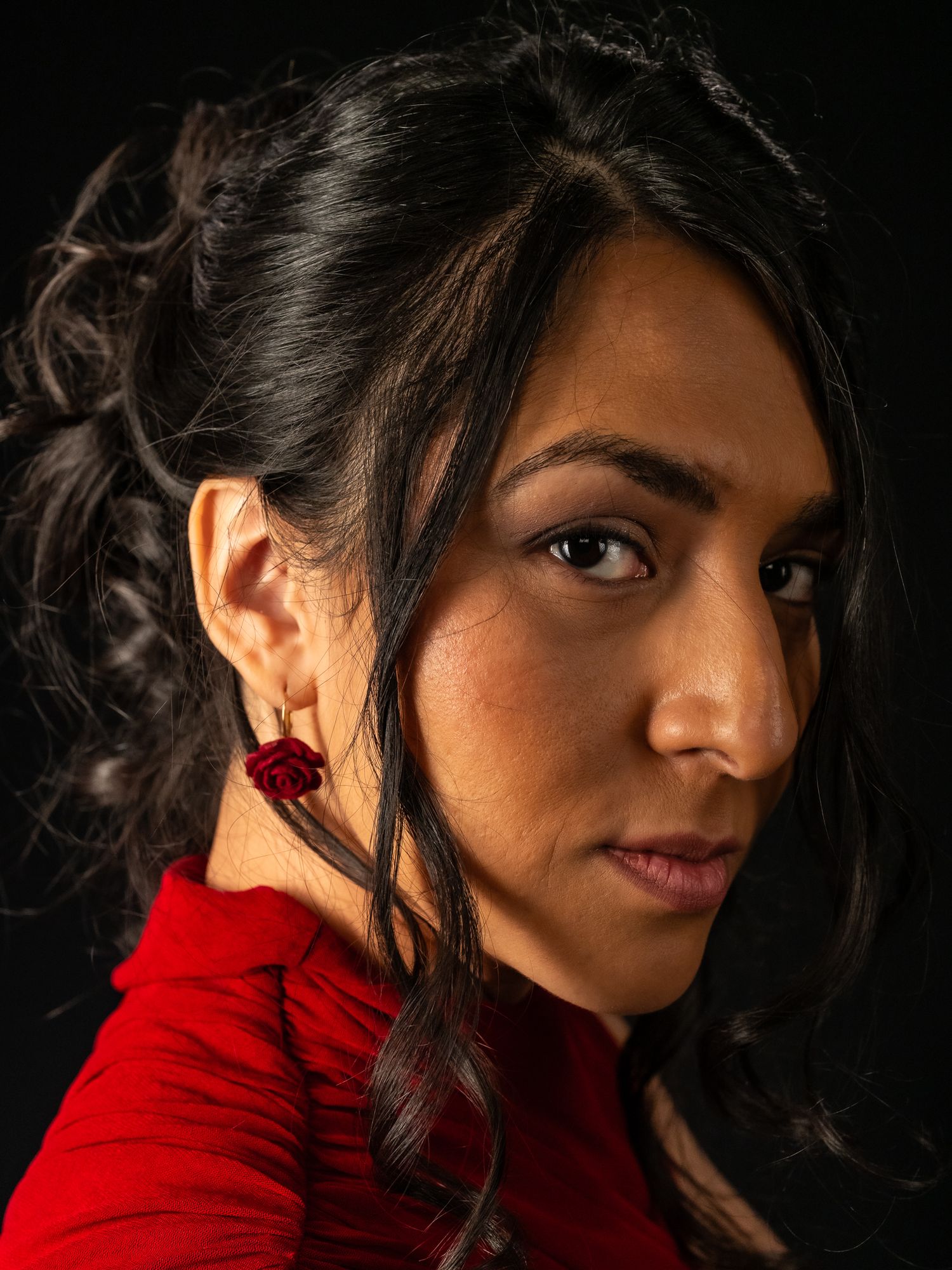A woman in a red dress with rose earrings poses against a dark background.