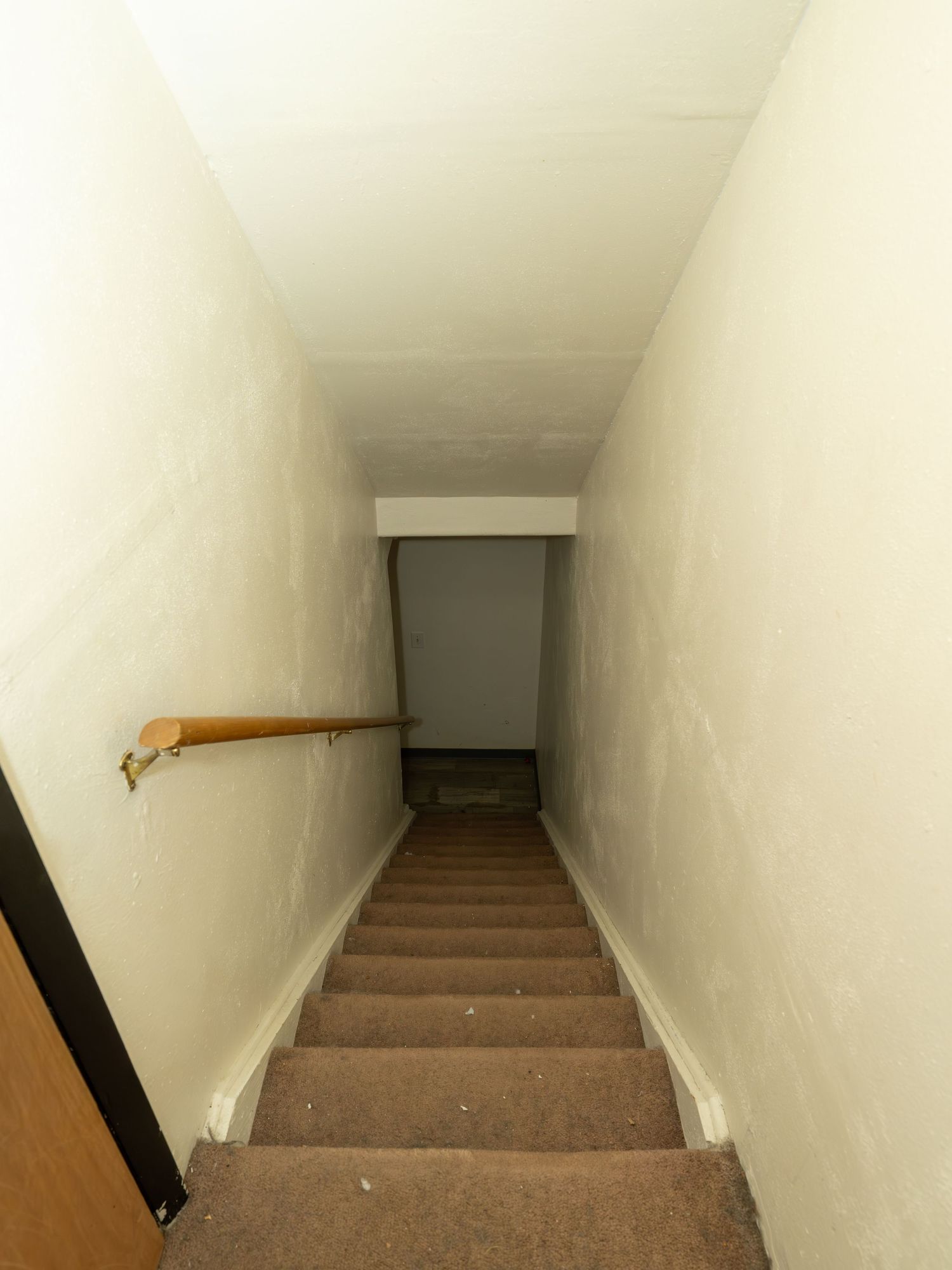 White-walled staircase leading down to basement with wooden handrail.