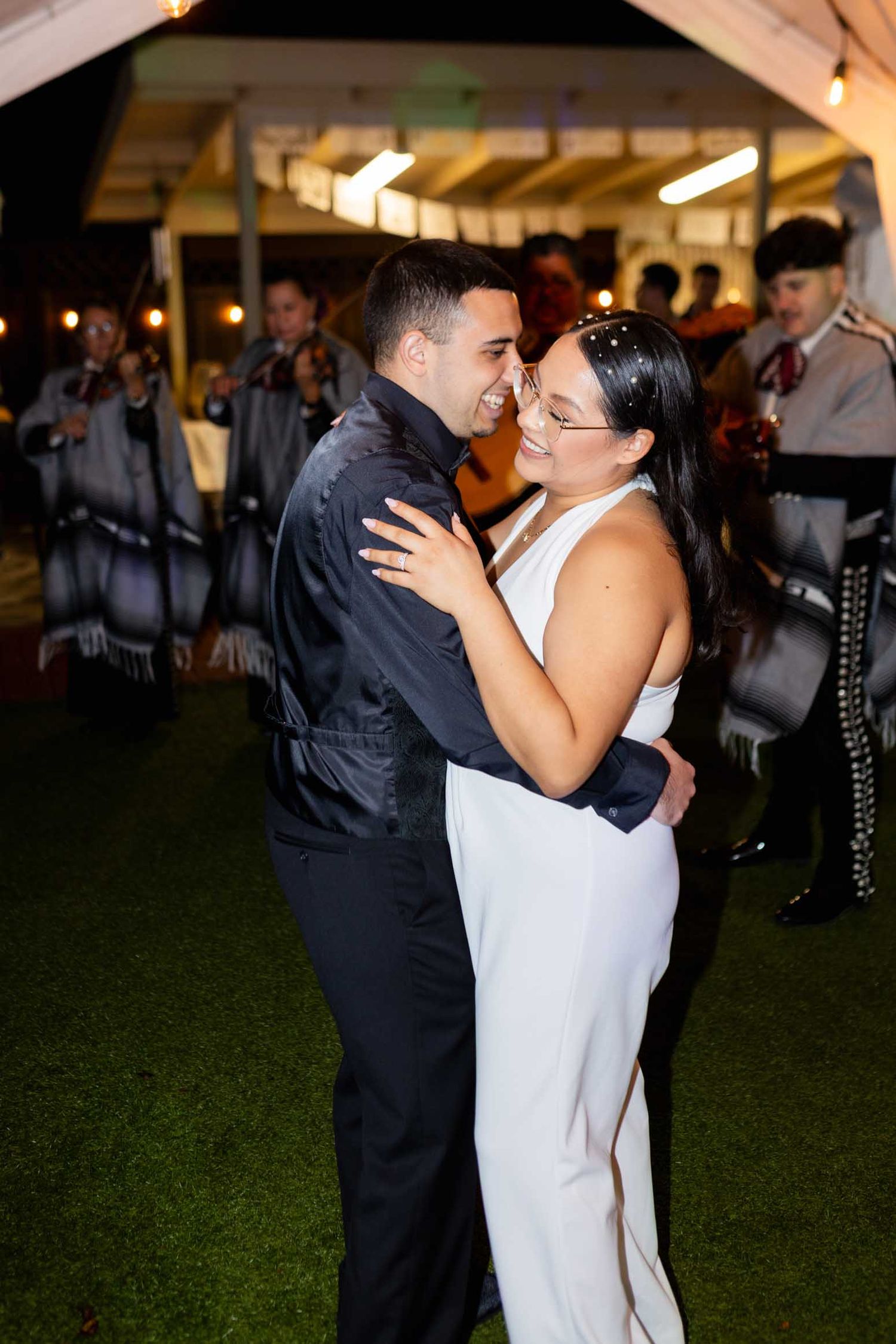A couple shares a romantic dance at an outdoor evening wedding reception under string lights.
