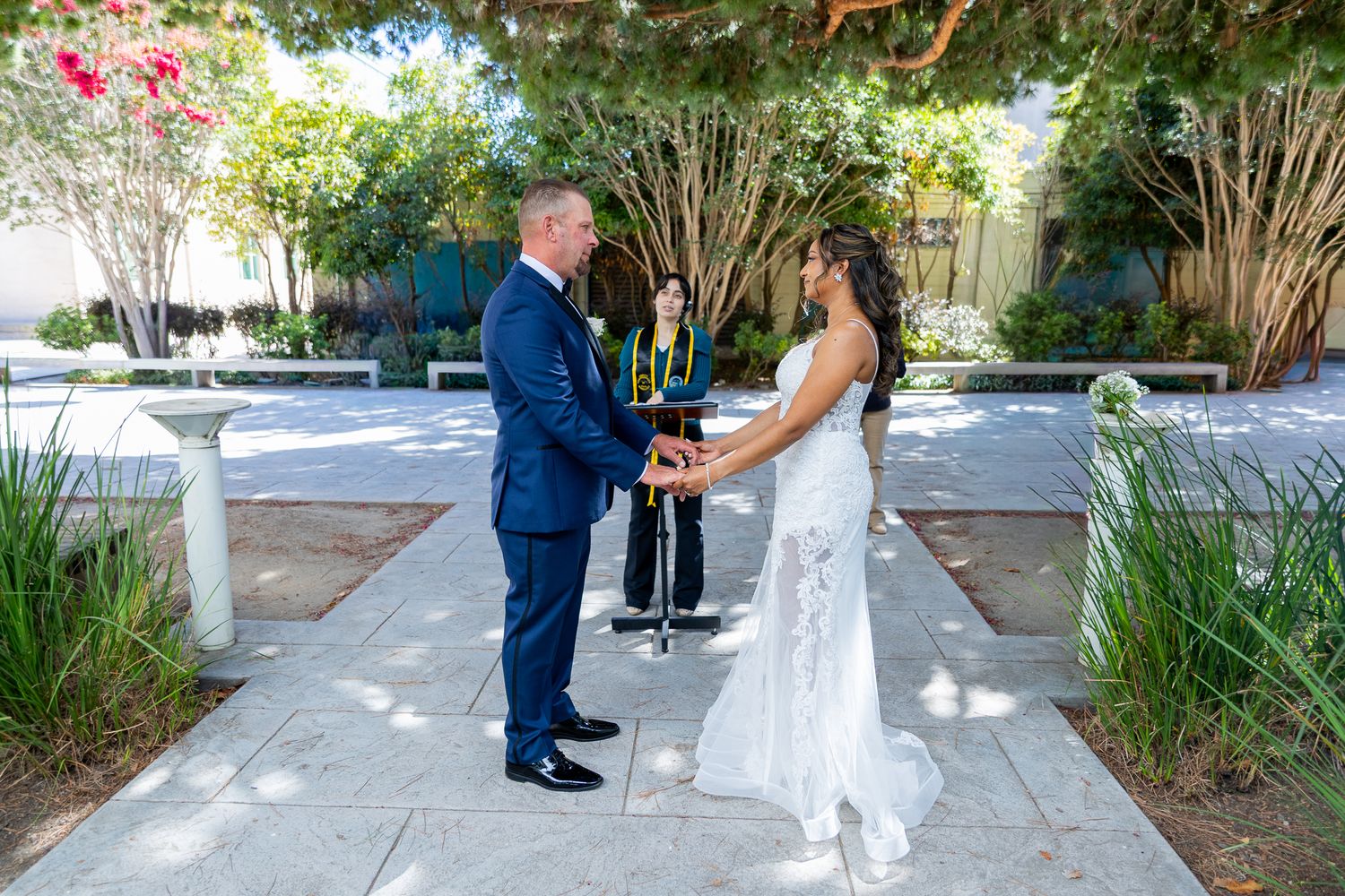 Couple exchanging vows outdoors at a garden wedding ceremony with officiant, bride in white gown and groom in navy suit.
