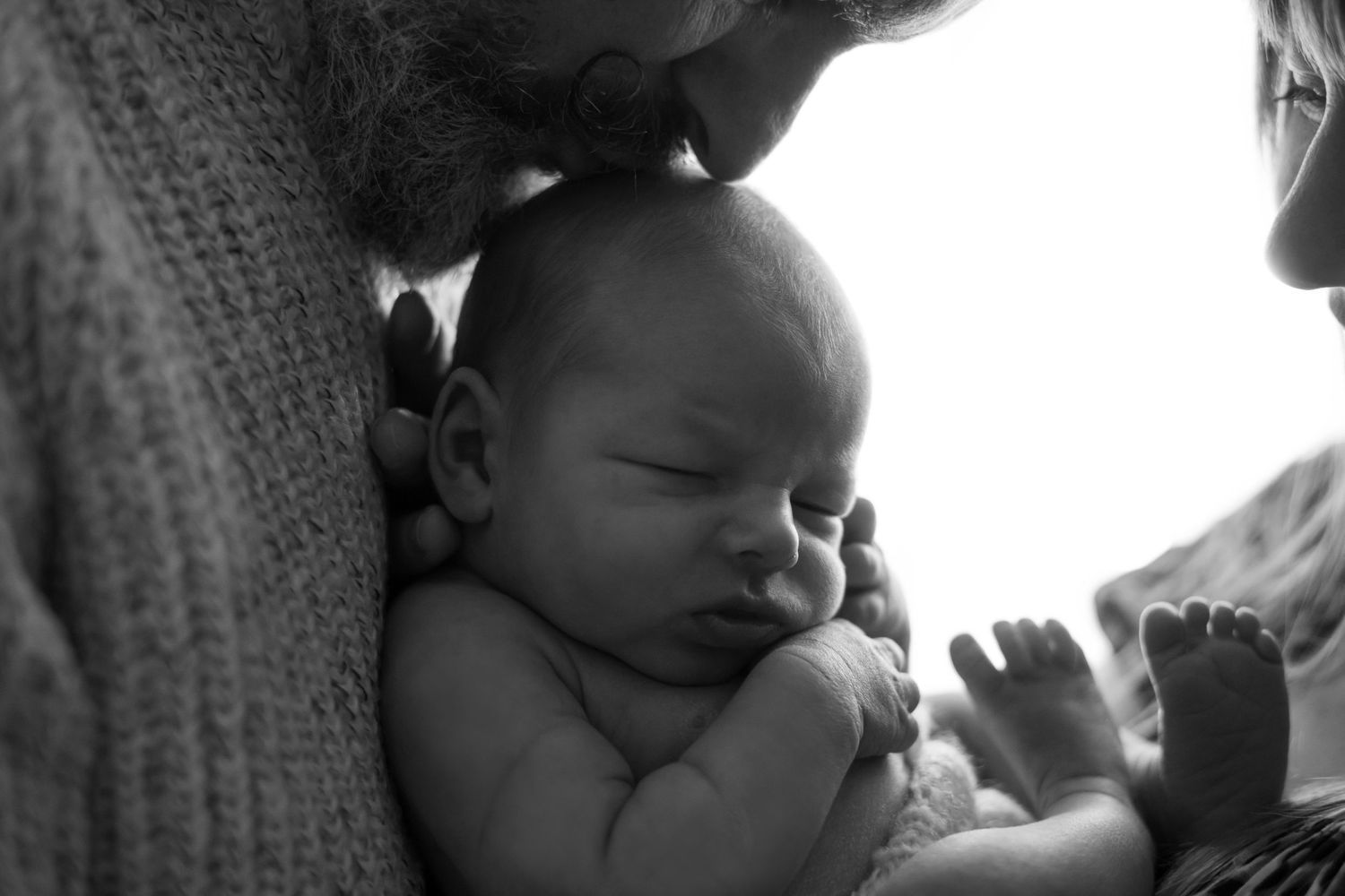 A peaceful sleeping newborn baby rests against it's father in a tender black and white portrait.