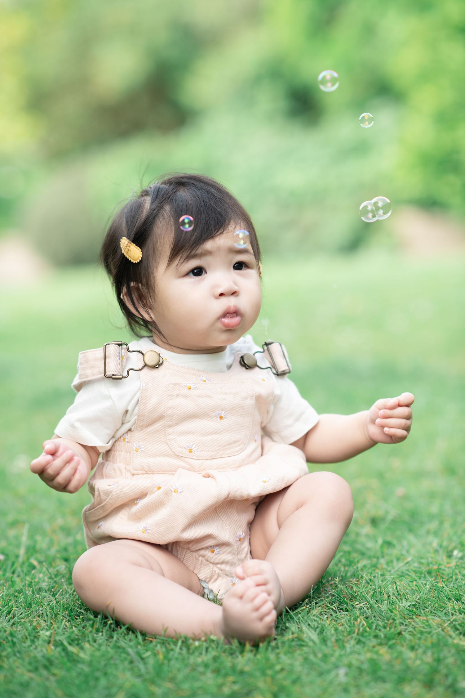 A baby sits on grass whilst bubbles fly past her