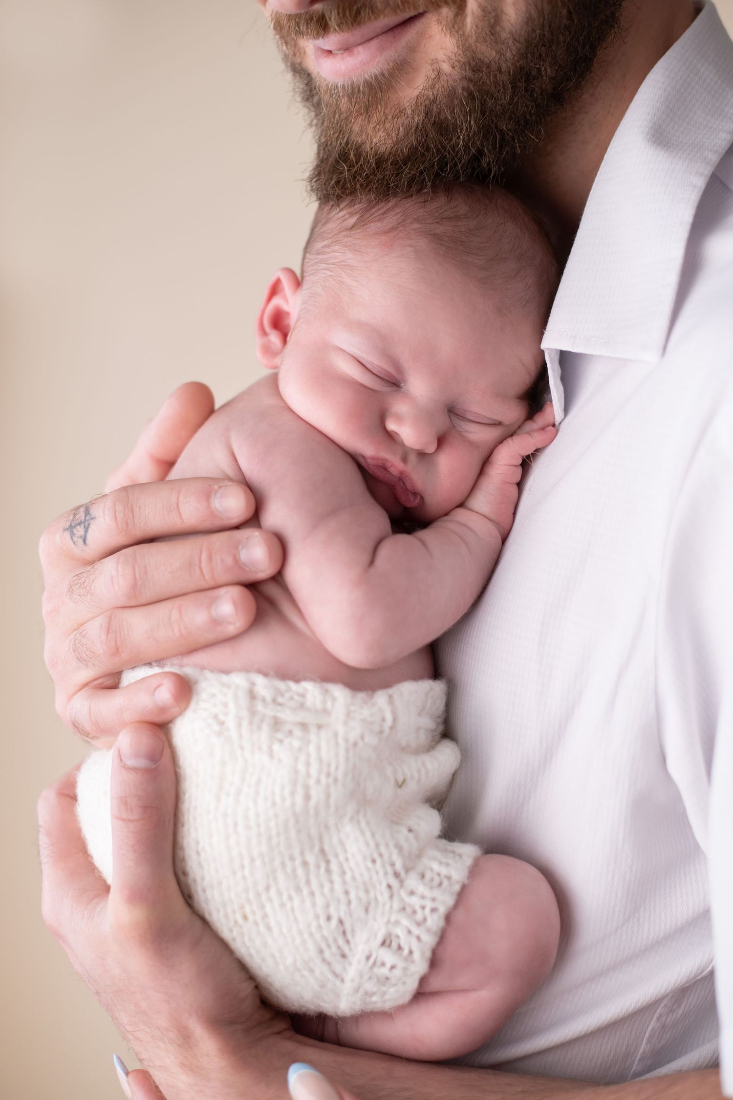 Newborn baby in cream shorts snuggled on dads chest with a cream background