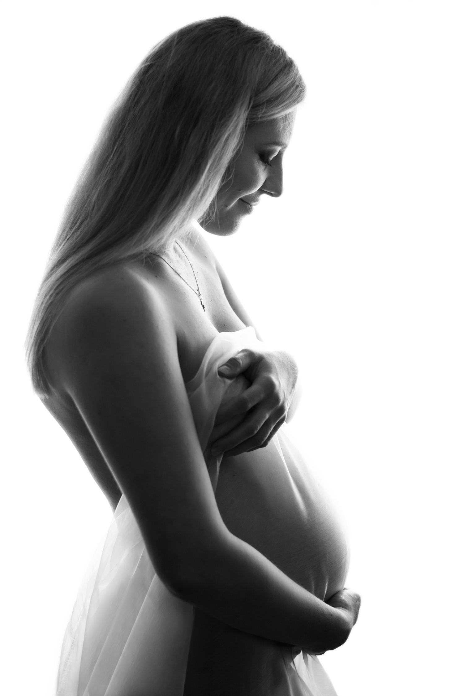 A black and white artistic maternity photo showing an expectant mother in profile against a light background.