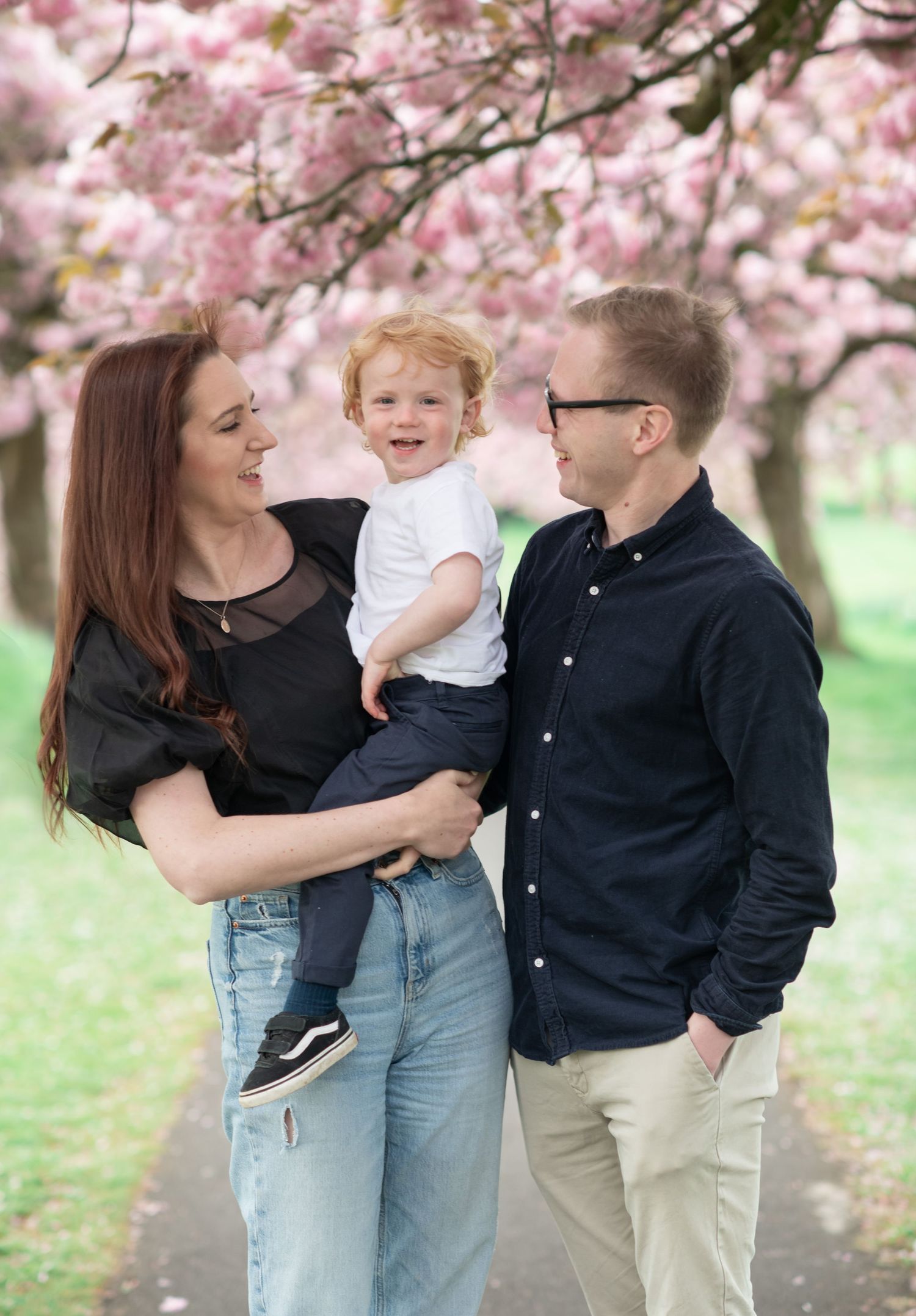 A mother and father hold their toddler amongst the cherry blossom trees in Harrogate
