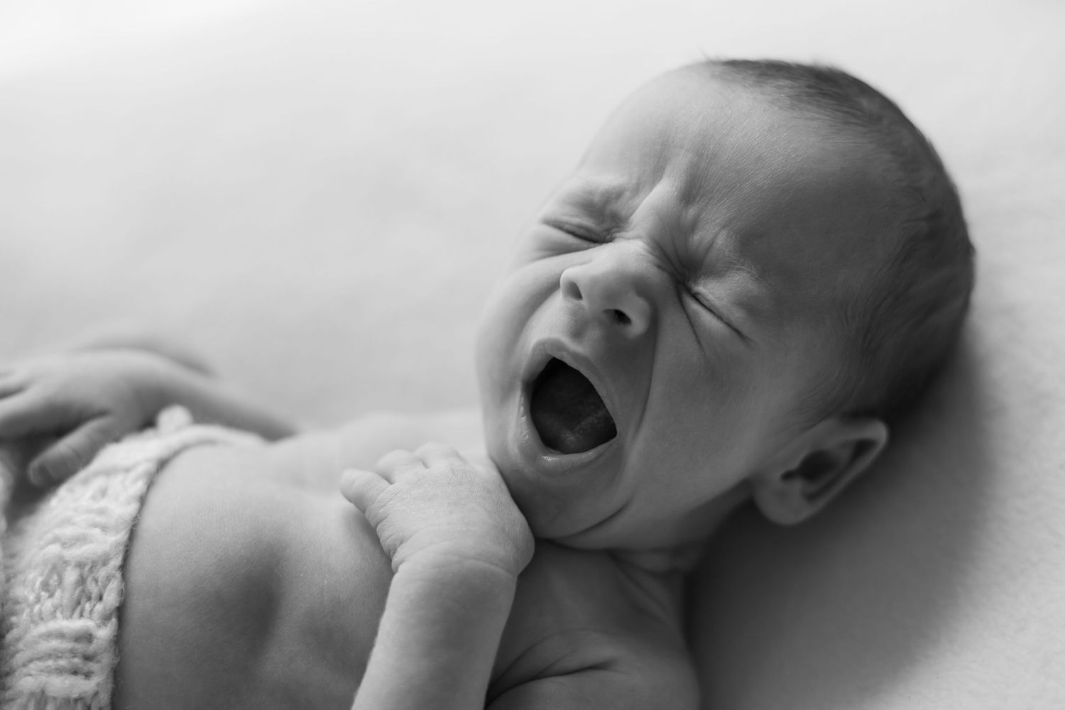Black and white photo of a yawning baby lying down on their back.
