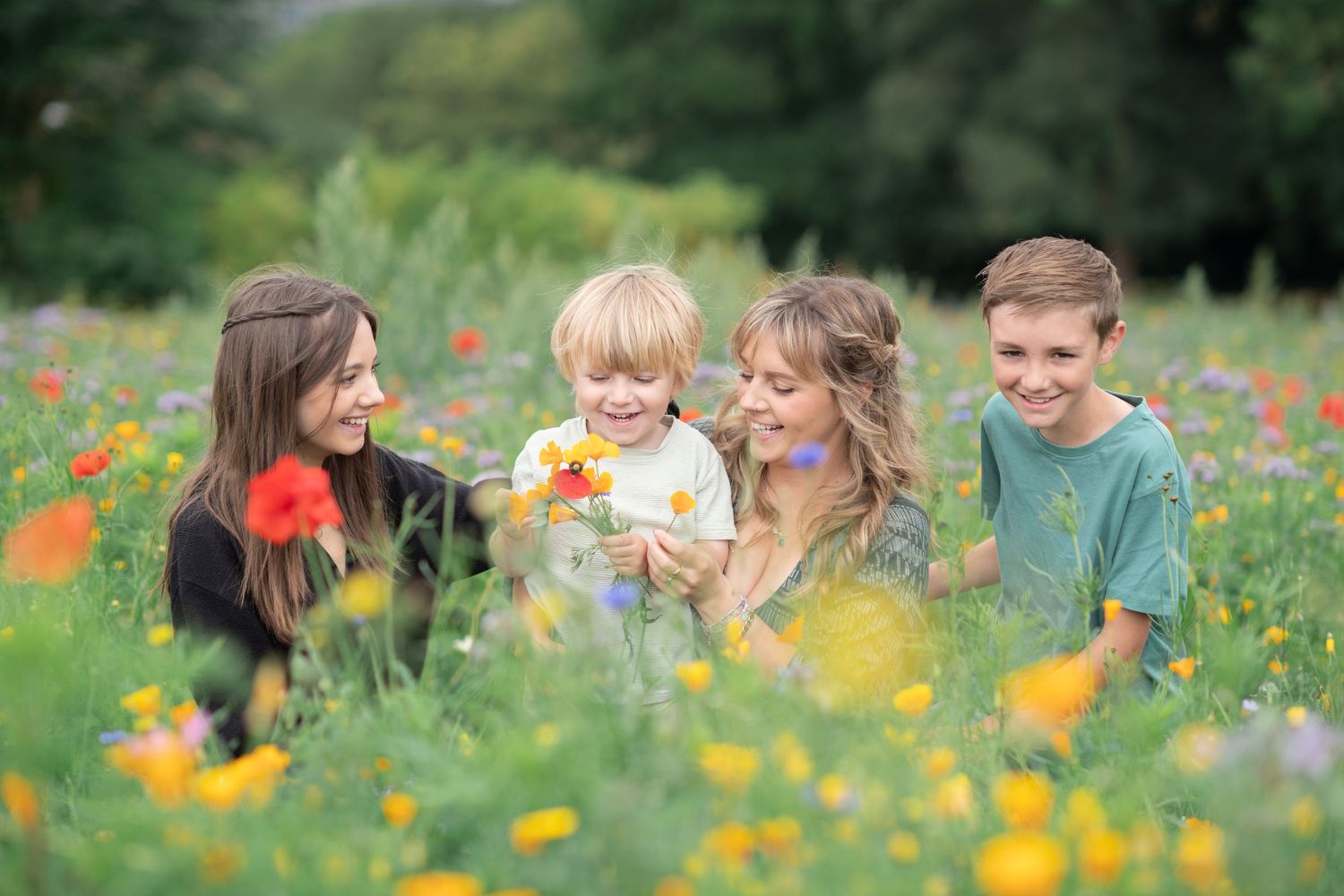 A family sits together in a vibrant wildflower meadow filled with orange poppies and yellow blooms on a sunny day.