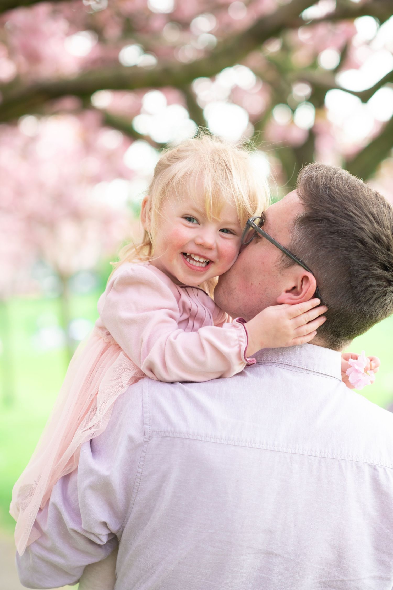 Parent and child share tender moments under blooming cherry blossoms in a series of joyful spring portraits.