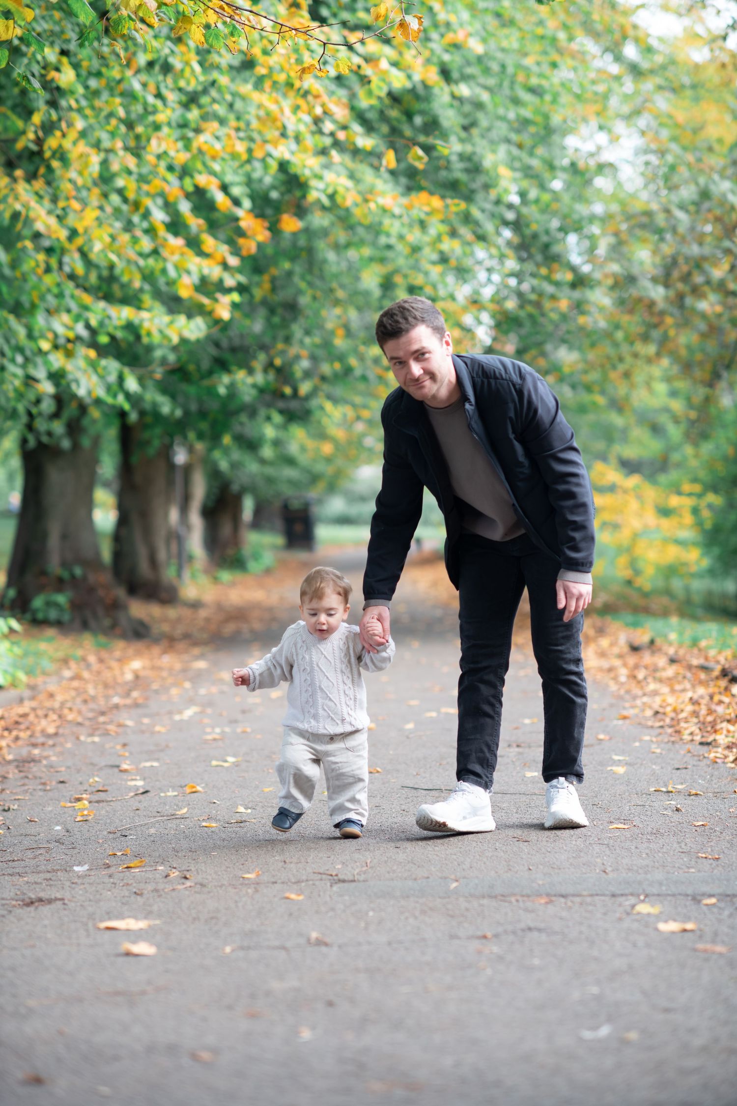 A father walking with his toddler in a Autumn setting with trees either side of the path