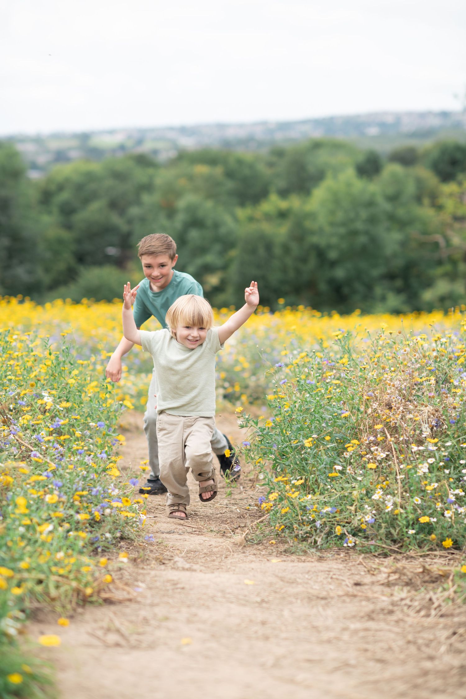 Children run and play along a dirt path through a vibrant yellow wildflower meadow on a sunny summer day.