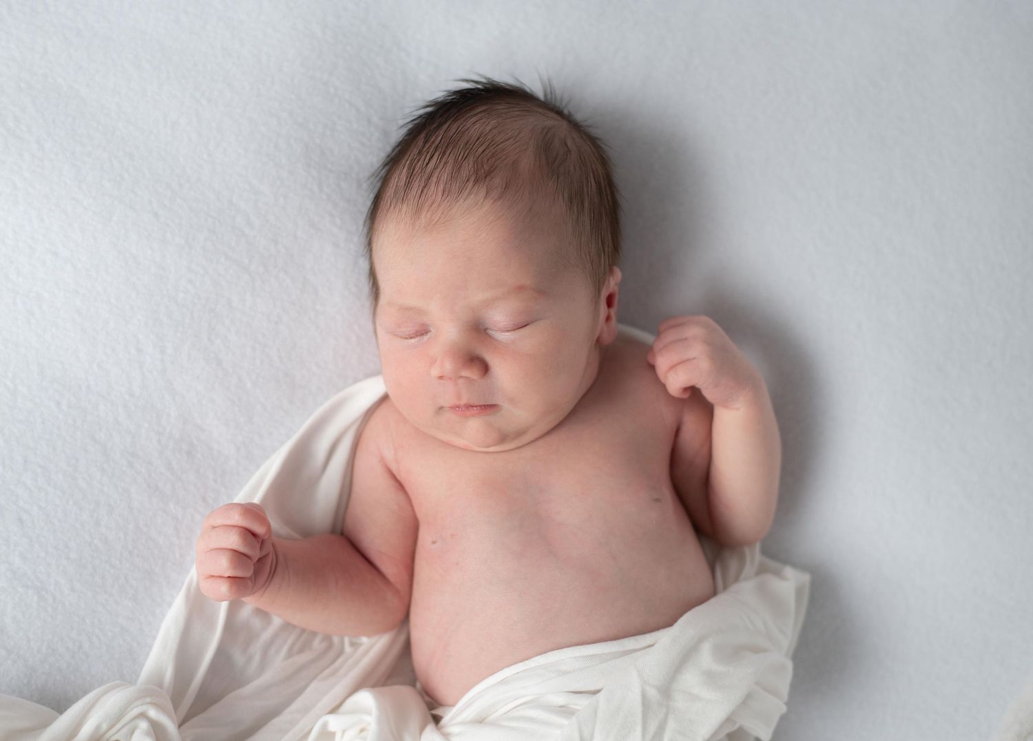 A newborn baby peacefully sleeping on white bedding with soft natural lighting.