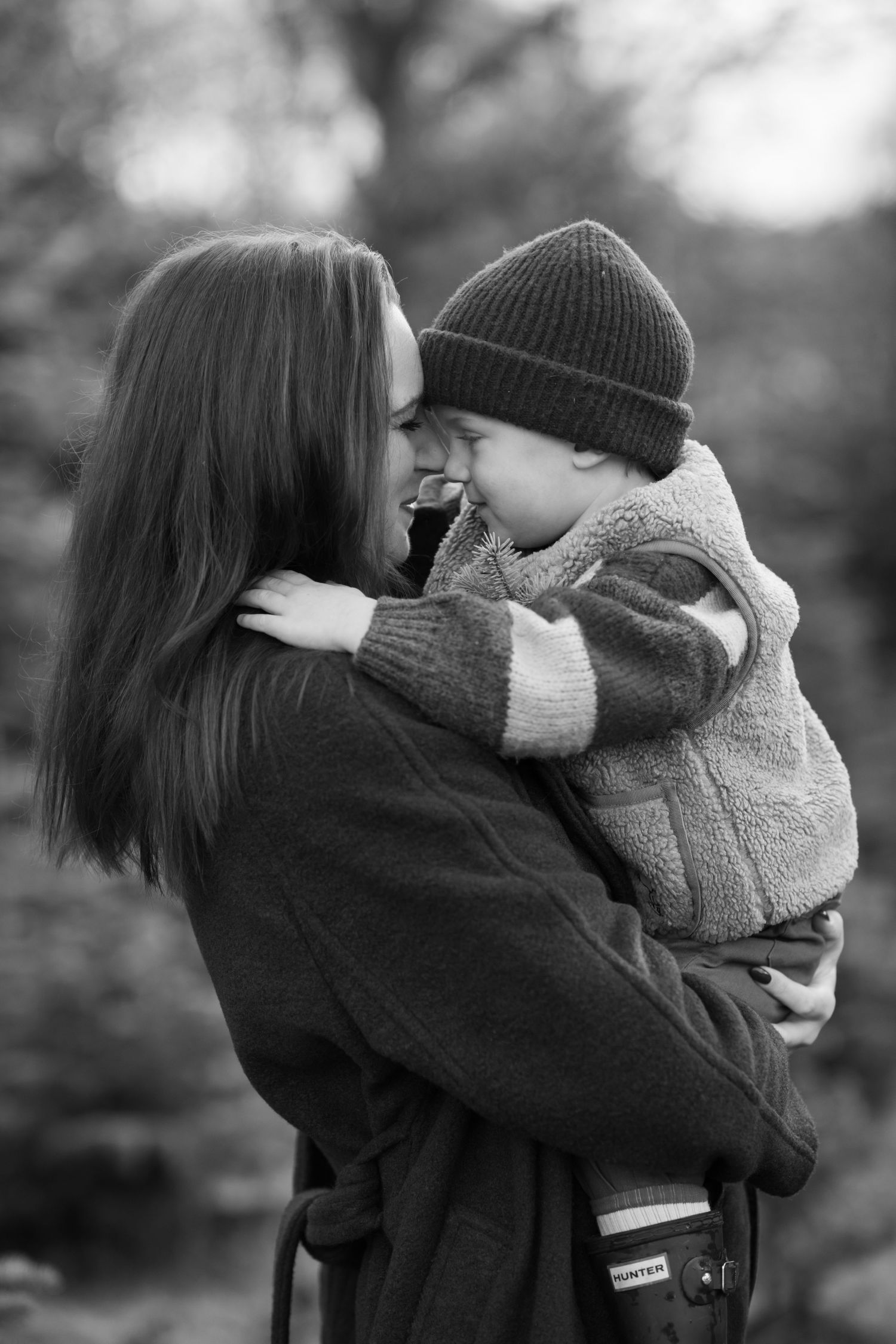 A beautiful black and white photo that shows a mother and son in winter clothing embracing and sharing a tender moment outdoors.