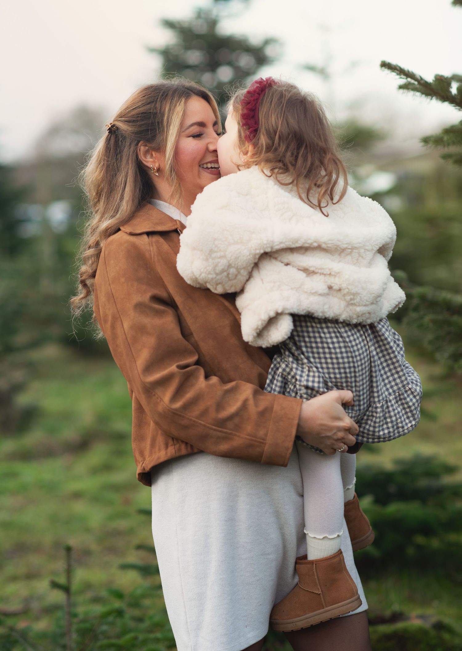 Mother and daughter embracing amongst Christmas trees