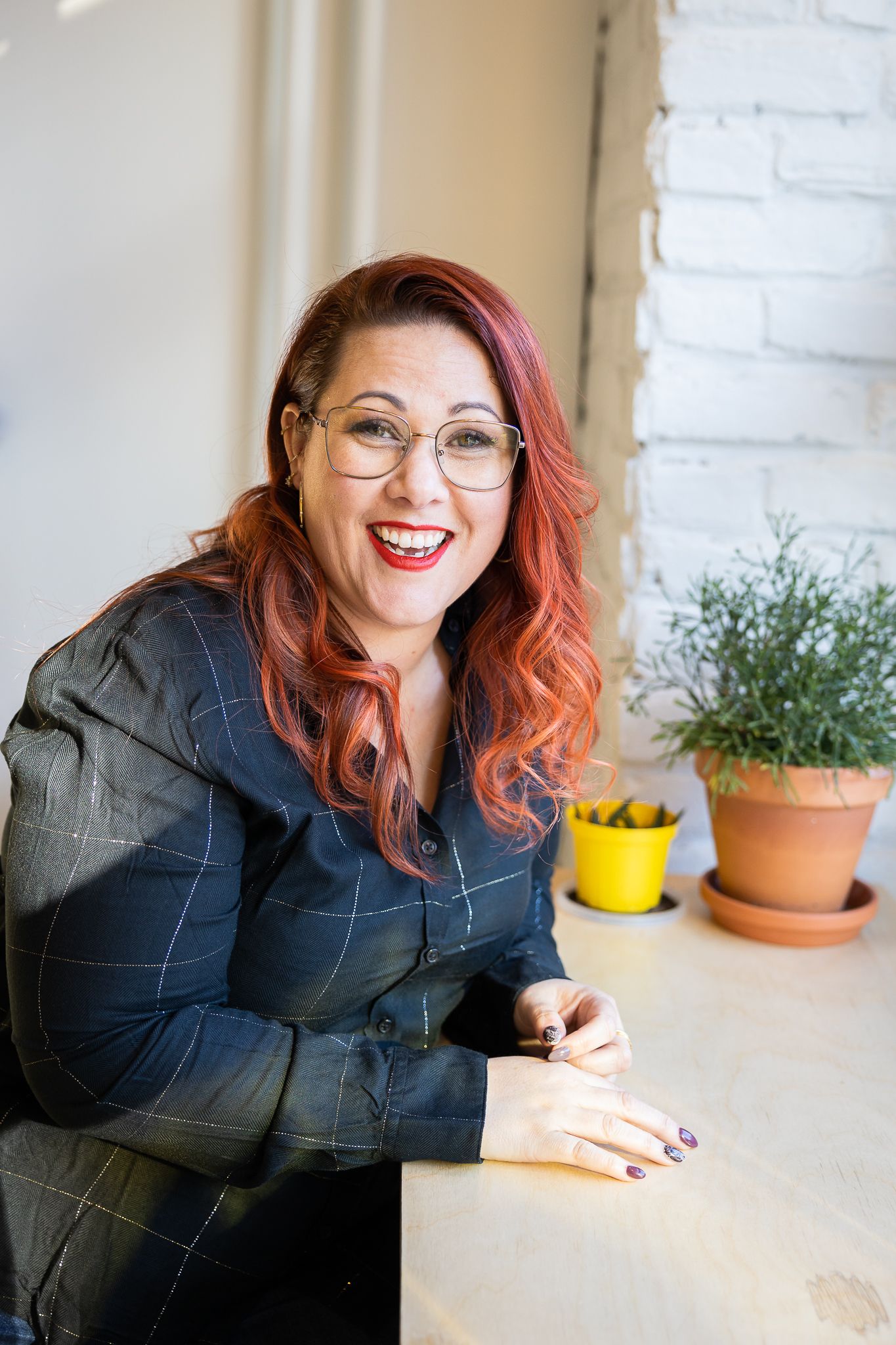 A series of photos showing someone with red hair and glasses smiling and gesturing while seated at a bright indoor space.