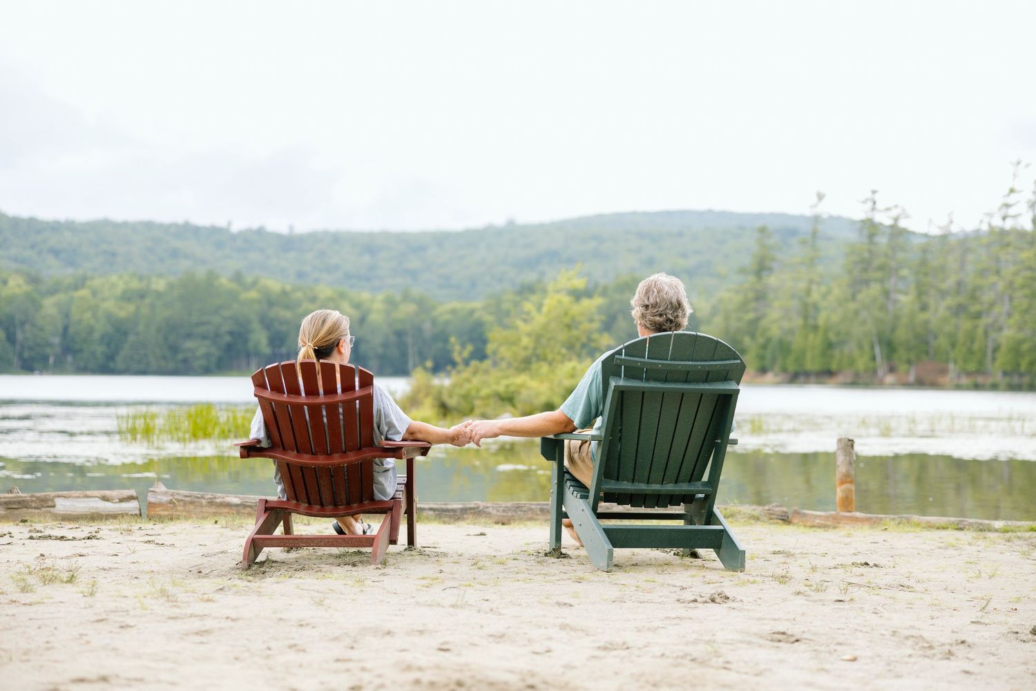 Two Adirondack chairs sit facing a peaceful lake view.