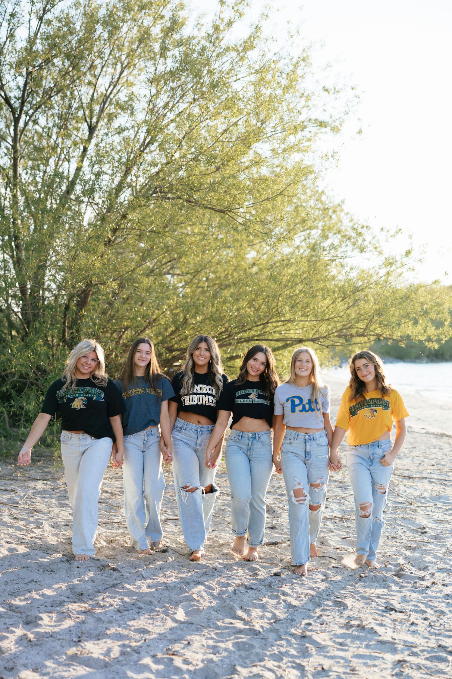 Beach photo of friends in college t-shirts walking on sandy shore at Hamlin Beach for high school graduation photos, Rochester, NY.