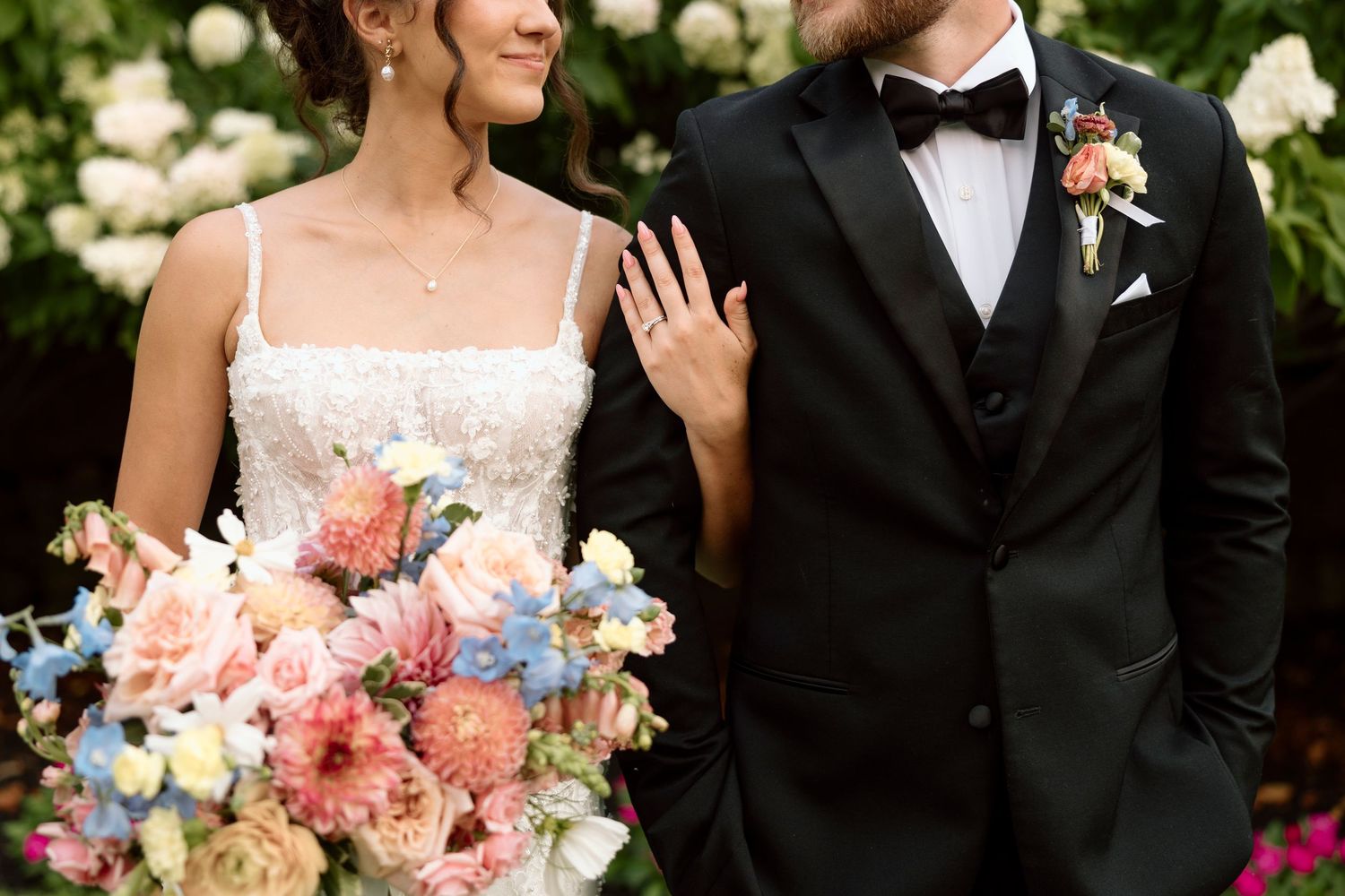 Elegant wedding couple with colorful bouquet featuring pink and blue flowers against floral backdrop at Shadow Lake in Victor, NY.