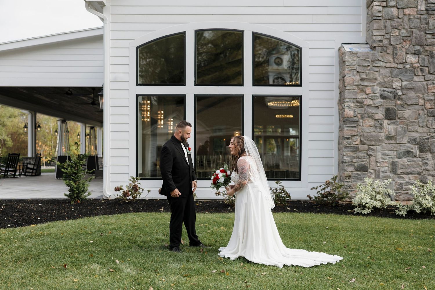 A wedding couple stands together on a manicured lawn in front of a white building with stone accents at Whitehall Mansion in brockport.