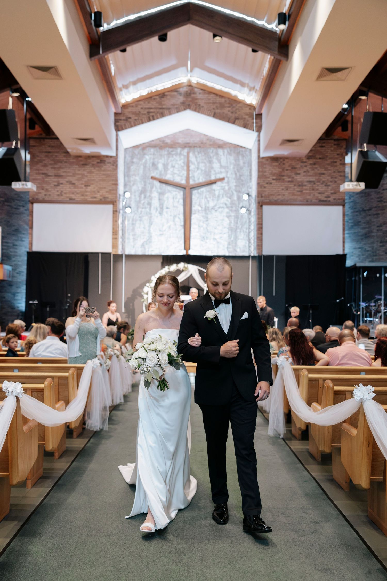 A church wedding ceremony with wooden pews and a cross illuminated by natural light from above at Hope Chruch in Rochester, NY wedding.