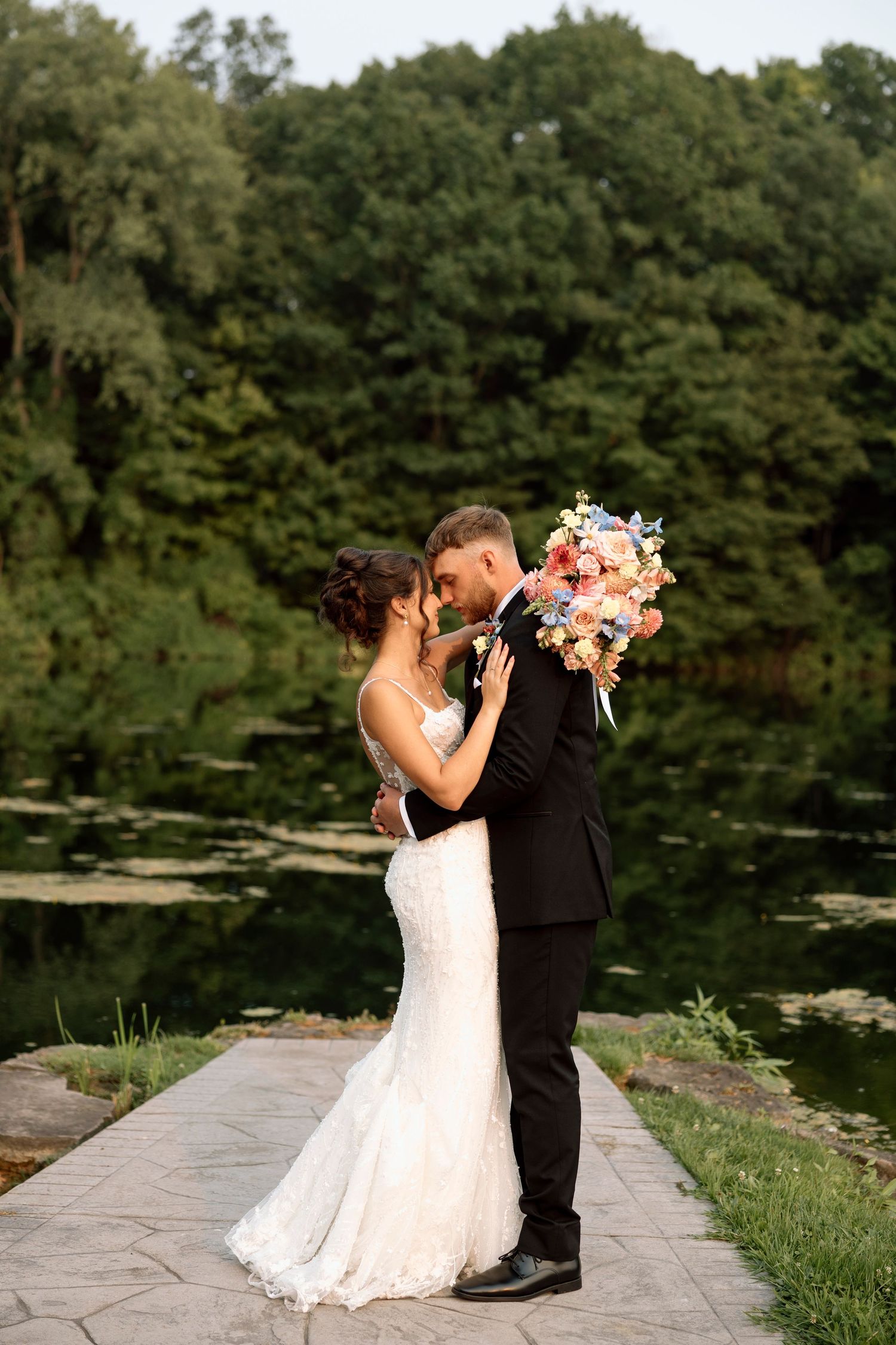 Romantic wedding portrait by Shadow Lake pond with lush greenery and colorful bouquet in summer wedding in Rochester, NY.