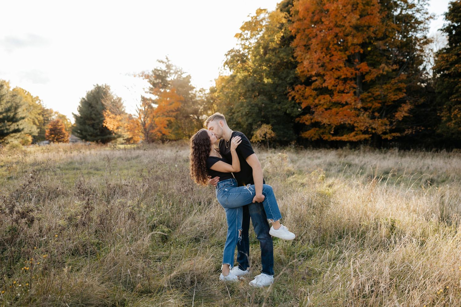 Couple walking together in autumn field with golden foliage in Rochester NY for engagement photos.