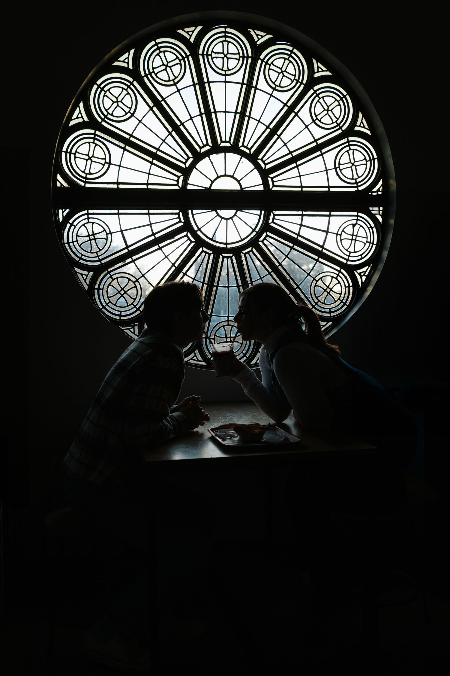 Ornate stained glass window with geometric patterns in a dark church setting behind a couple.