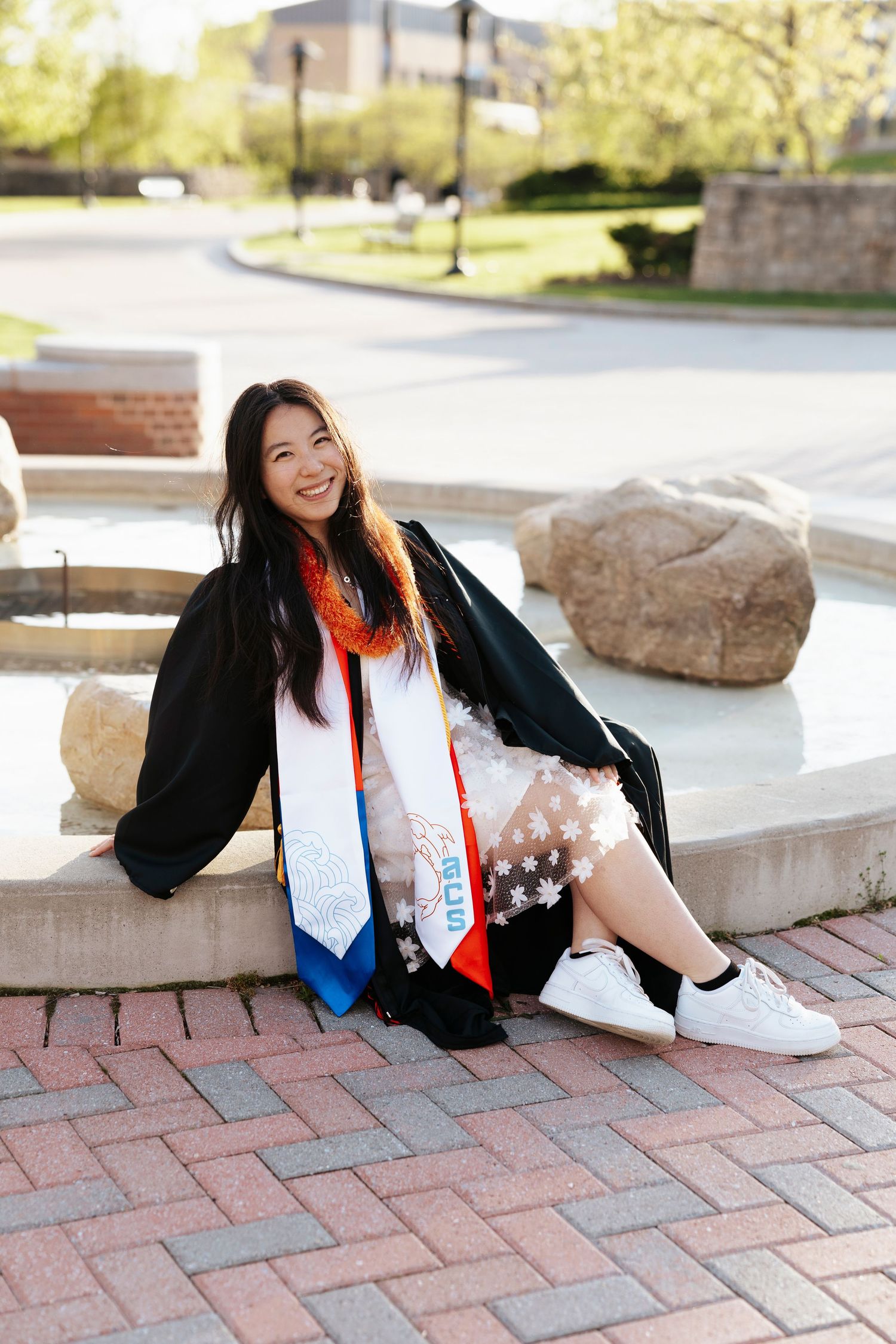 Graduate in cap and gown poses on brick pavement with decorative stoles at Rochester Institute of Technology for Rochester NY grad photos.