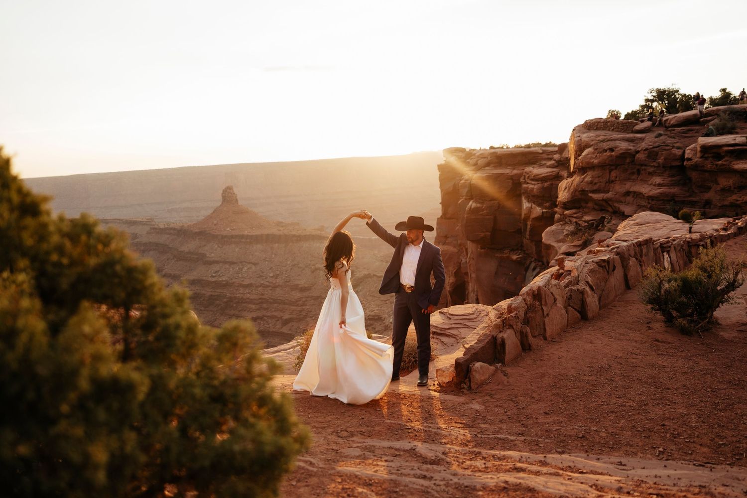 Couple in wedding attire holding hands on desert cliff edge at golden hour for Moab, Utah Dead Horse Point elopement.