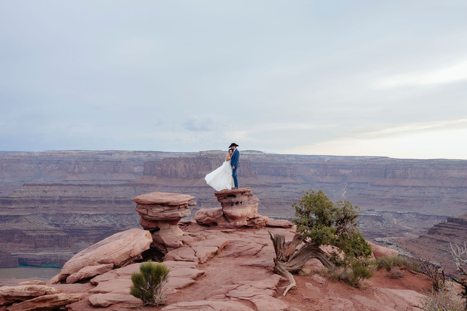 A bride and groom are standing on dramatic red rock overlook at Dead Horse Point State Park during their Utah elopement.