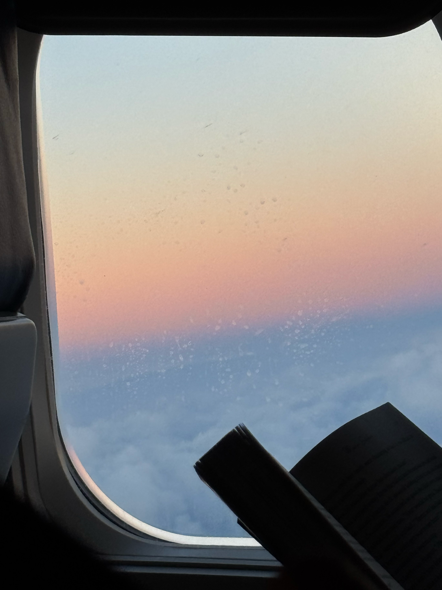 Airplane window view of a stunning pink and blue sunset above the clouds during a flight.