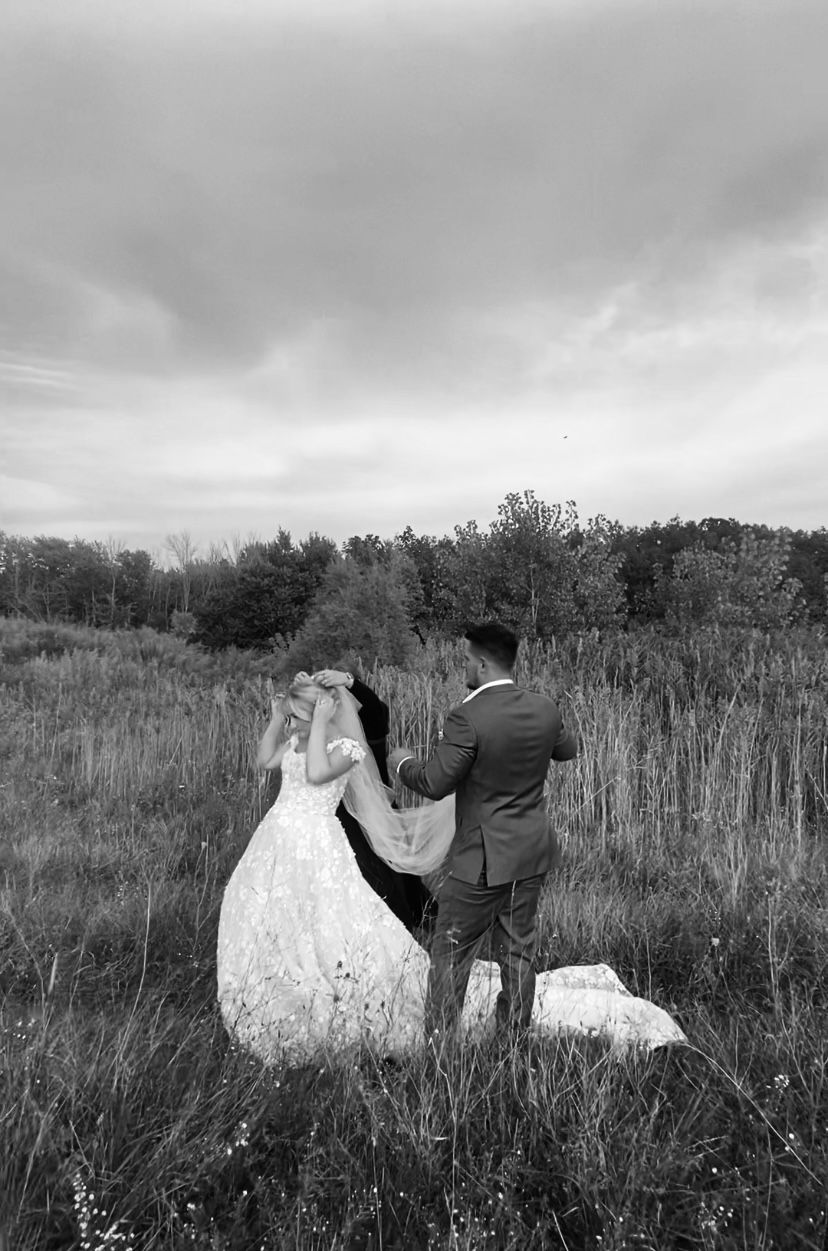 A couple poses together in a scenic field with dramatic cloudy skies.