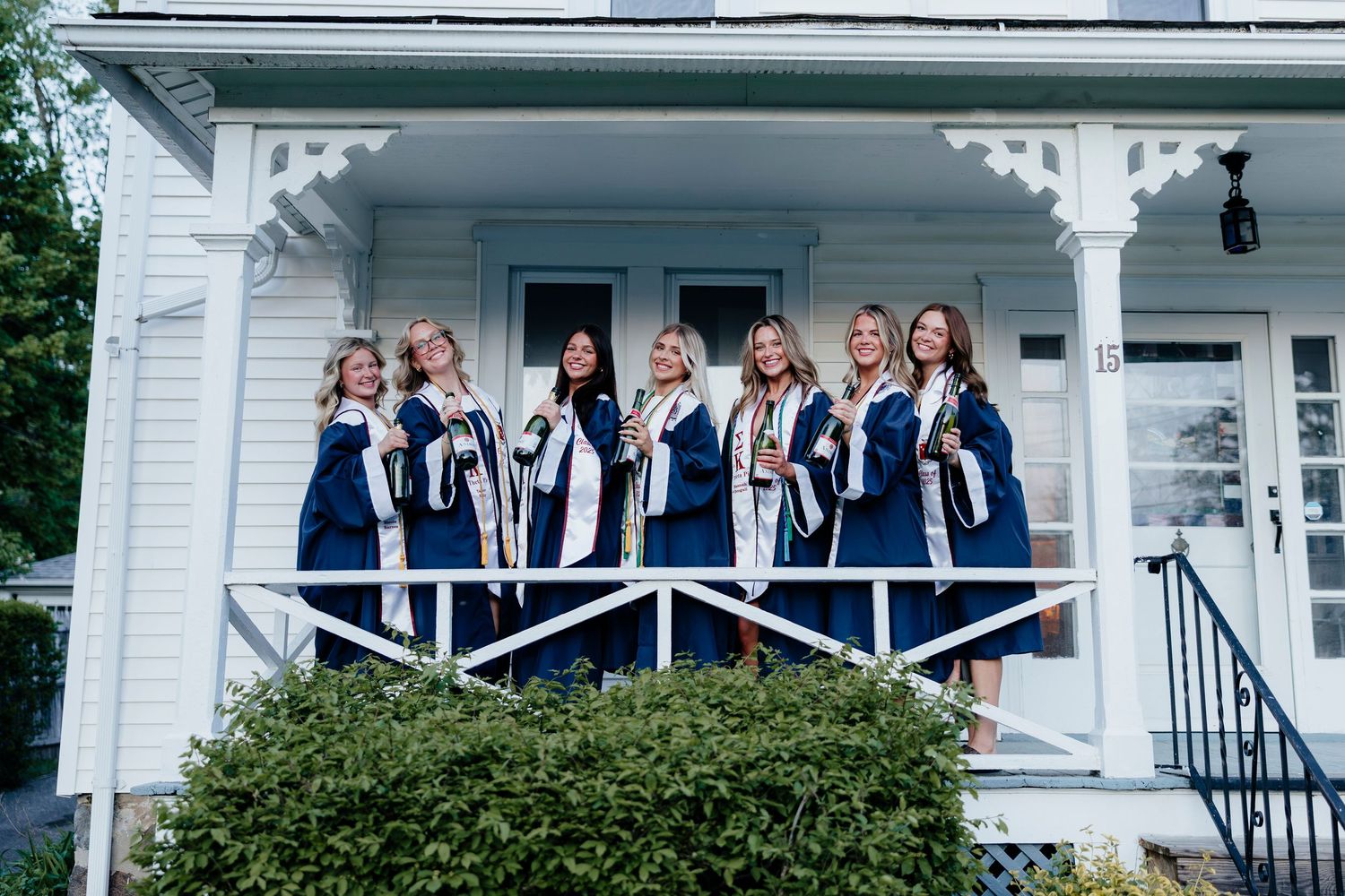 Group photos of people in navy graduation gowns posing on a white college house porch with decorative trim.