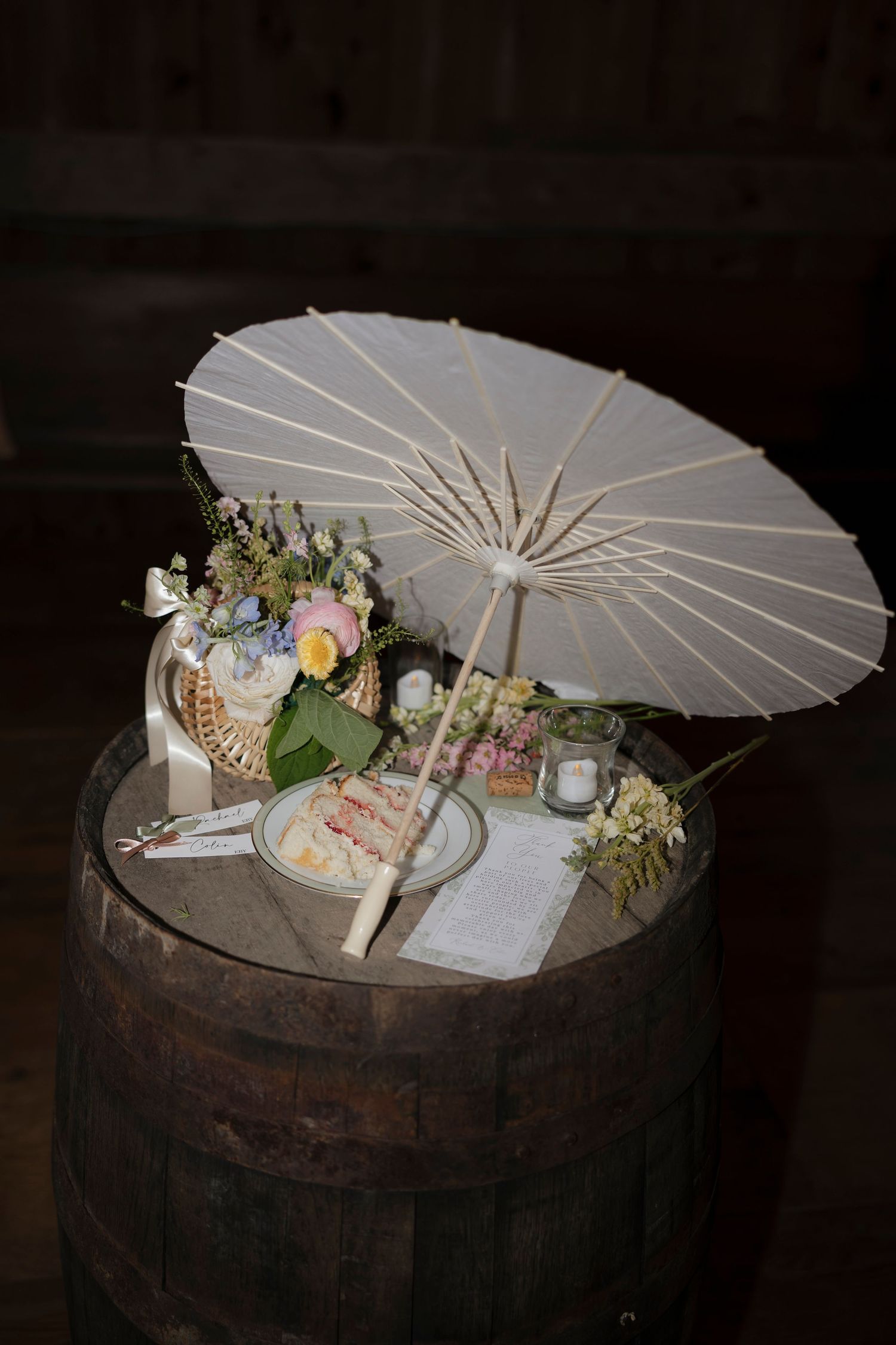Late night flash photo of decorative white parasols, cake, and floral arrangements displayed on rustic wooden barrel in Rochester NY wedding