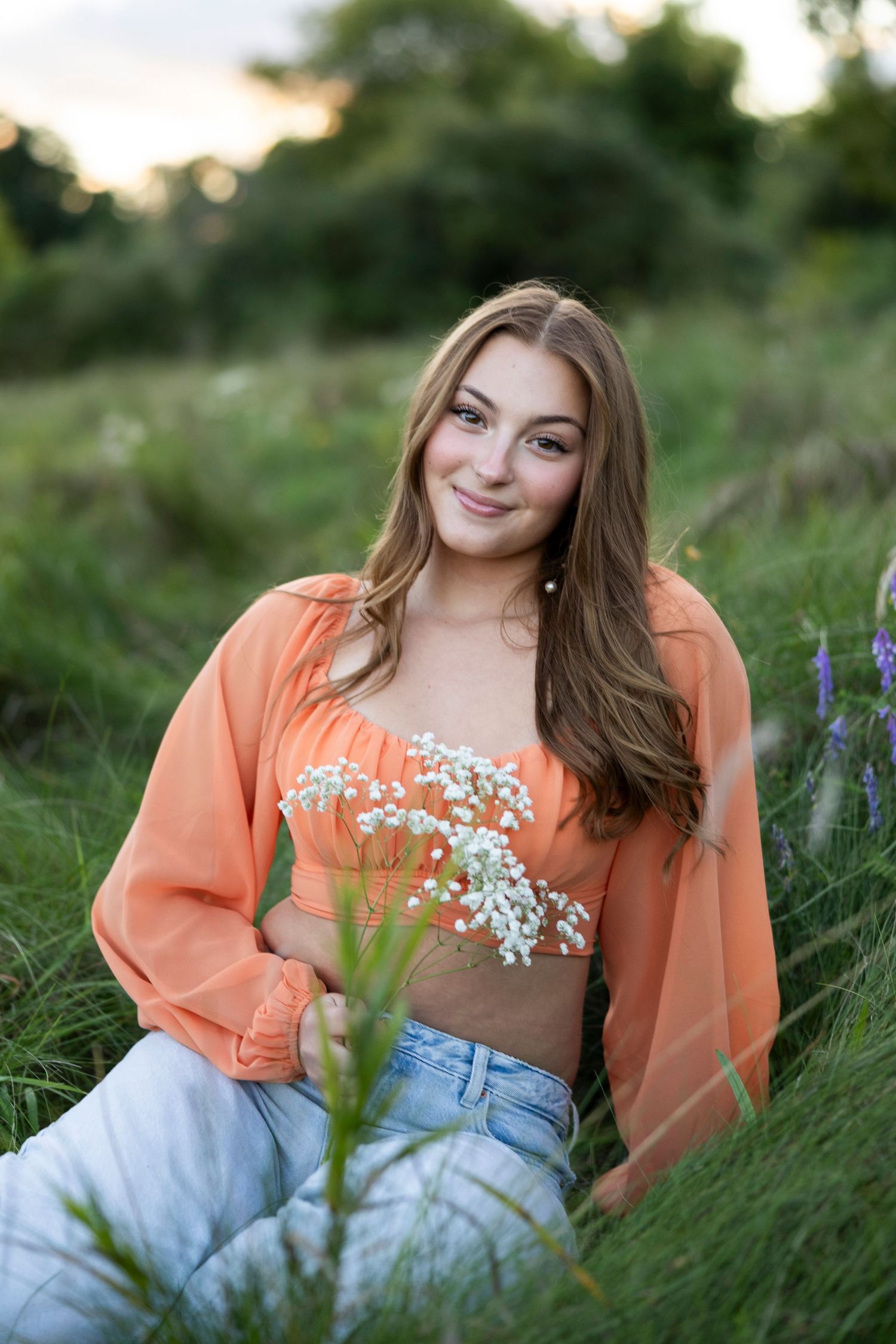 Outdoor portrait with orange top and jeans among wildflowers in golden light at Hamlin beach for Rochester, NY senior photos.