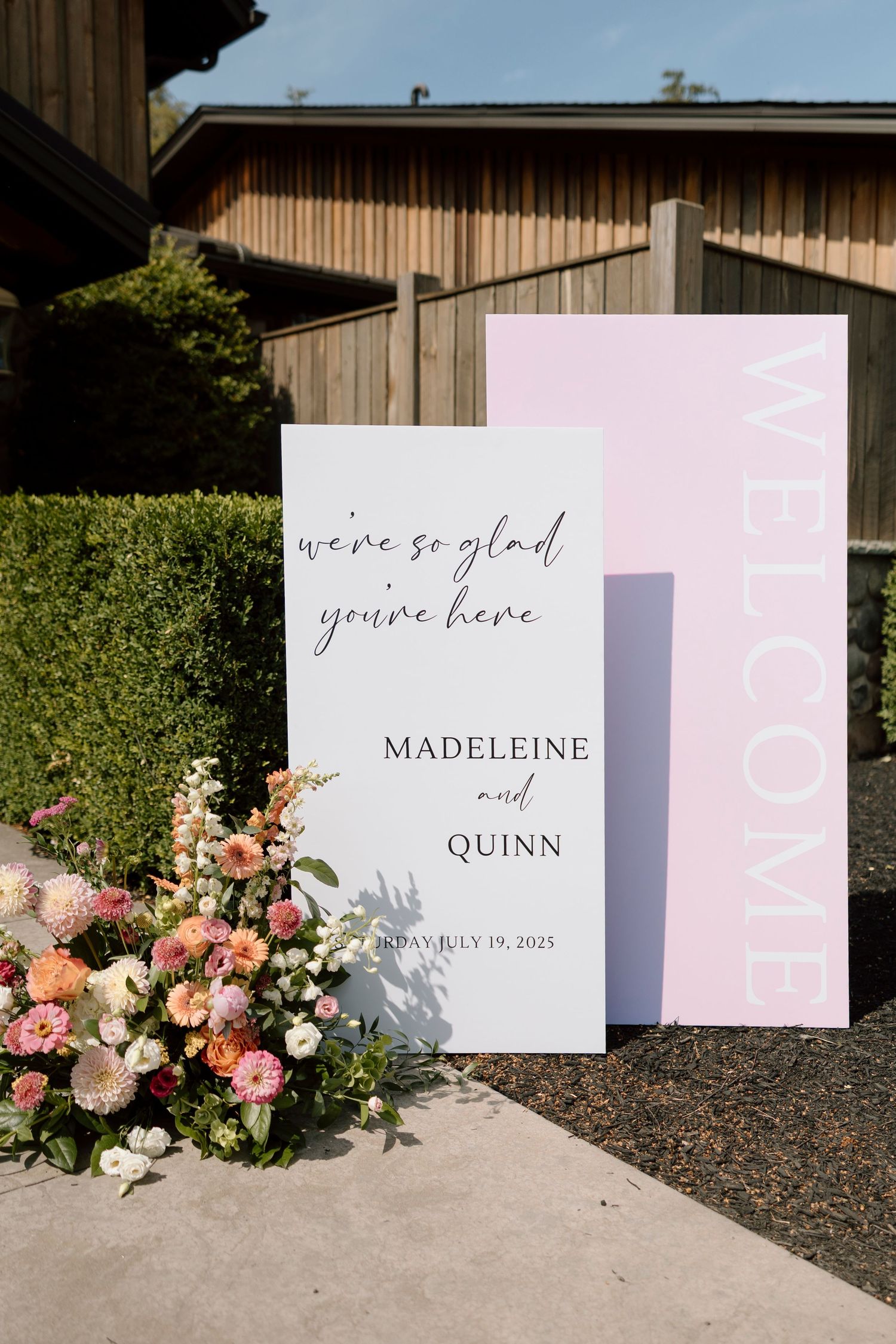 Wedding welcome sign with pink and white floral arrangements displayed against a wooden barn wall in Wilson NY for wedding reception.