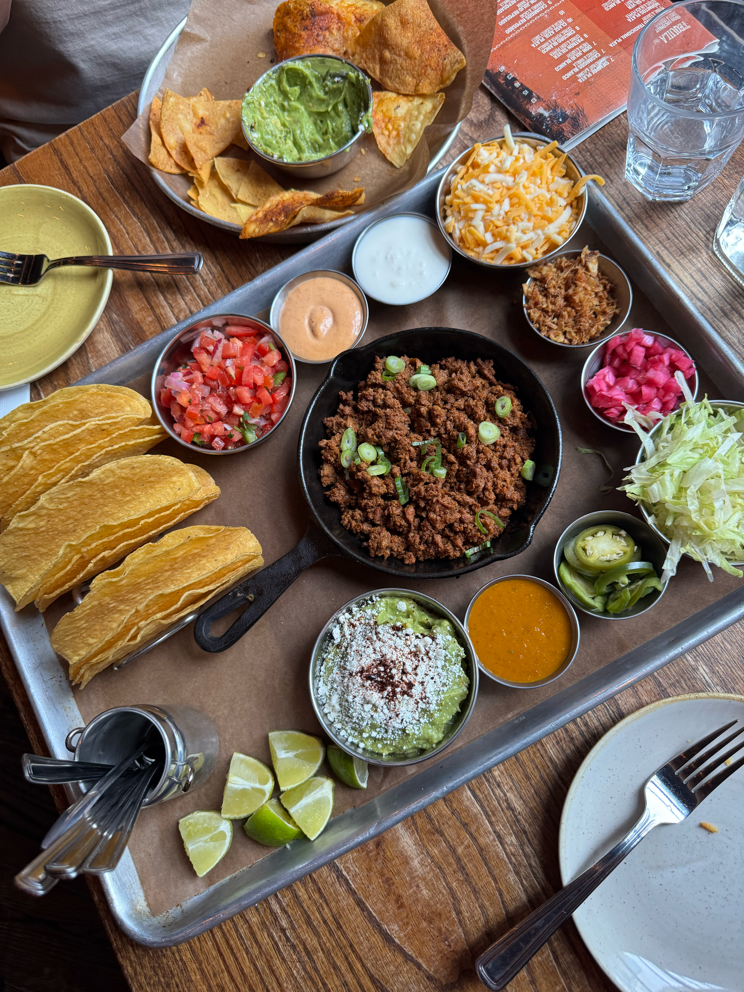 An array of Mexican taco toppings and ingredients laid out on a rustic wooden table.