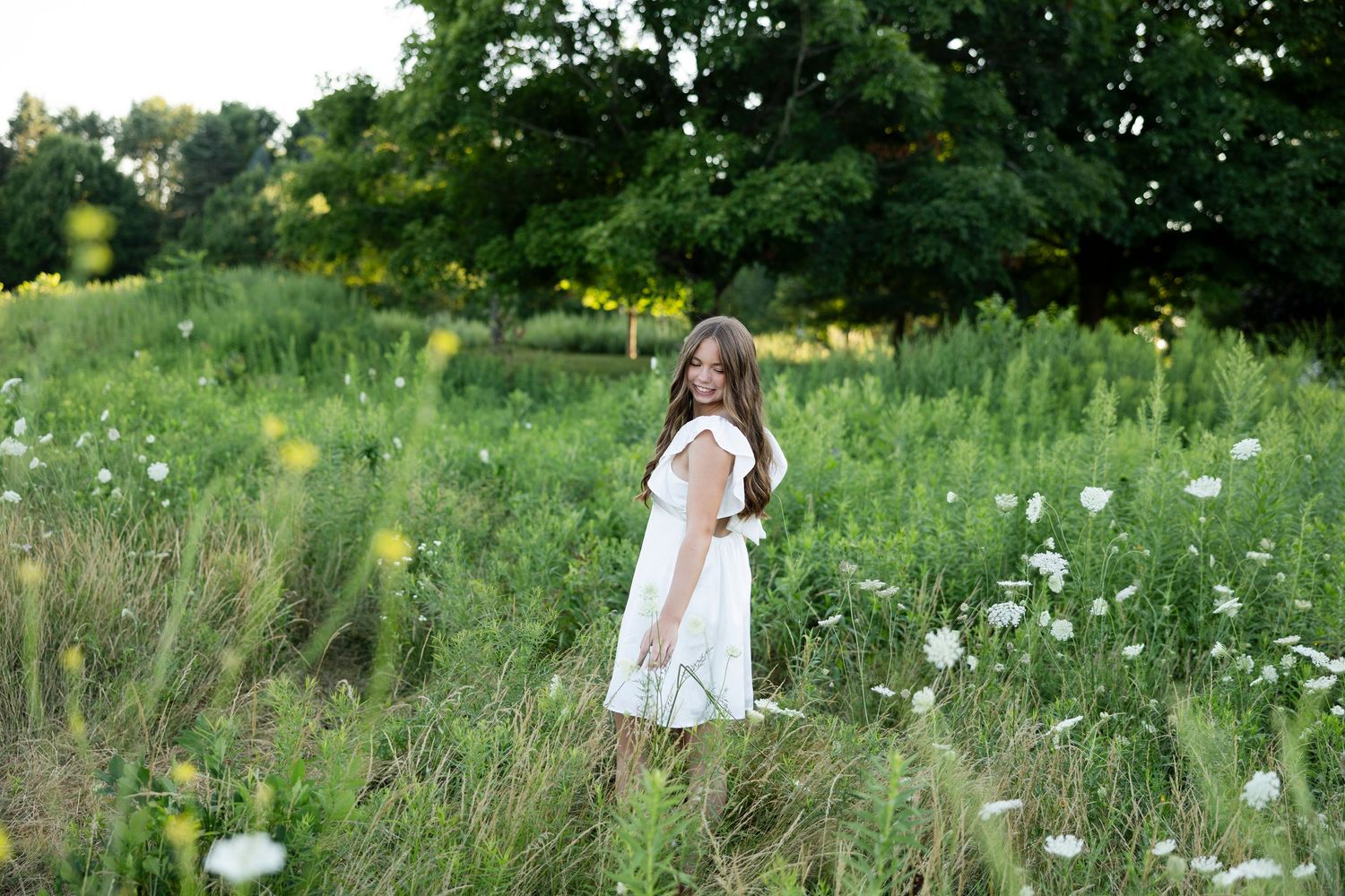 Ethereal portrait session in a wildflower meadow with a female high school senior wearing a white flowing dress.