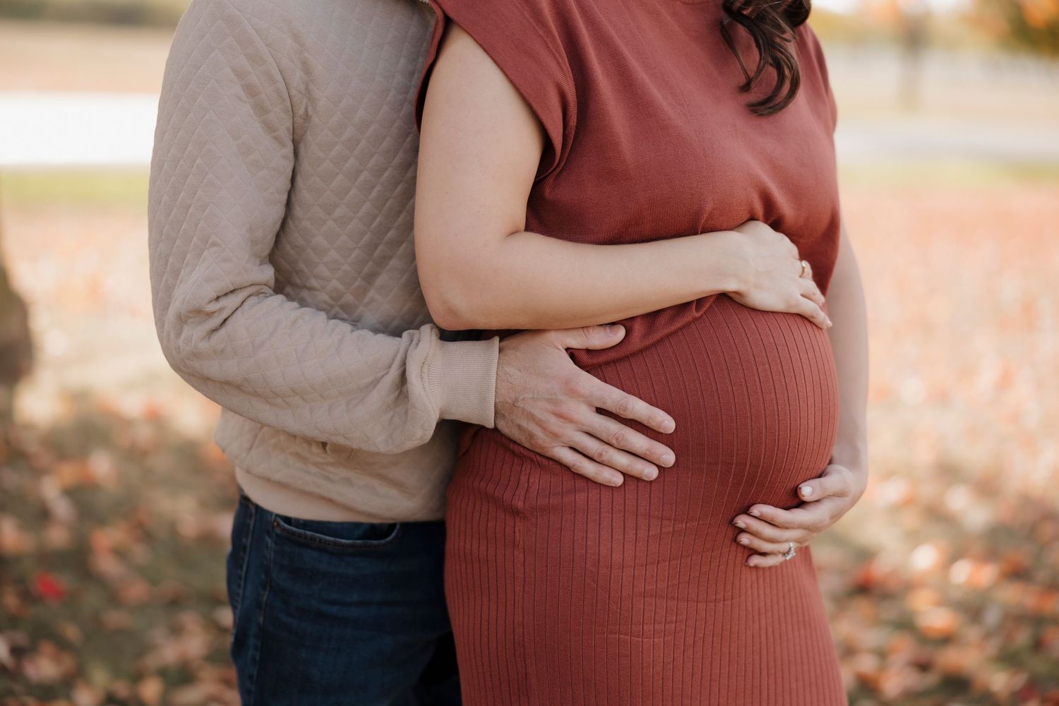 Close up view of a couple embracing, with one wearing a rust-colored dress for maternity photos in Rochester, NY.
