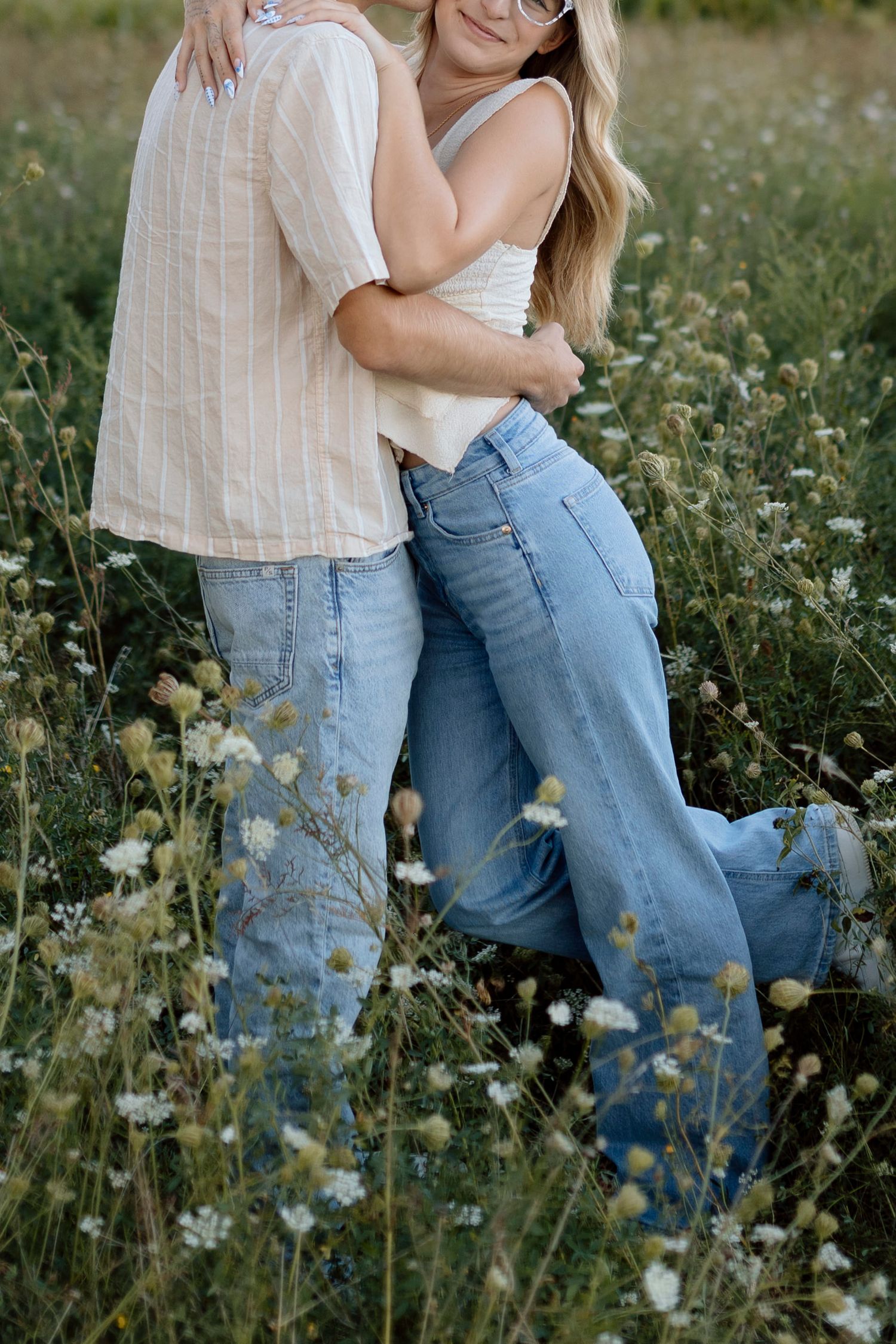 A romantic couple standing in a wildflower field wearing casual denim and white clothing in Avon NY for couples portaits.