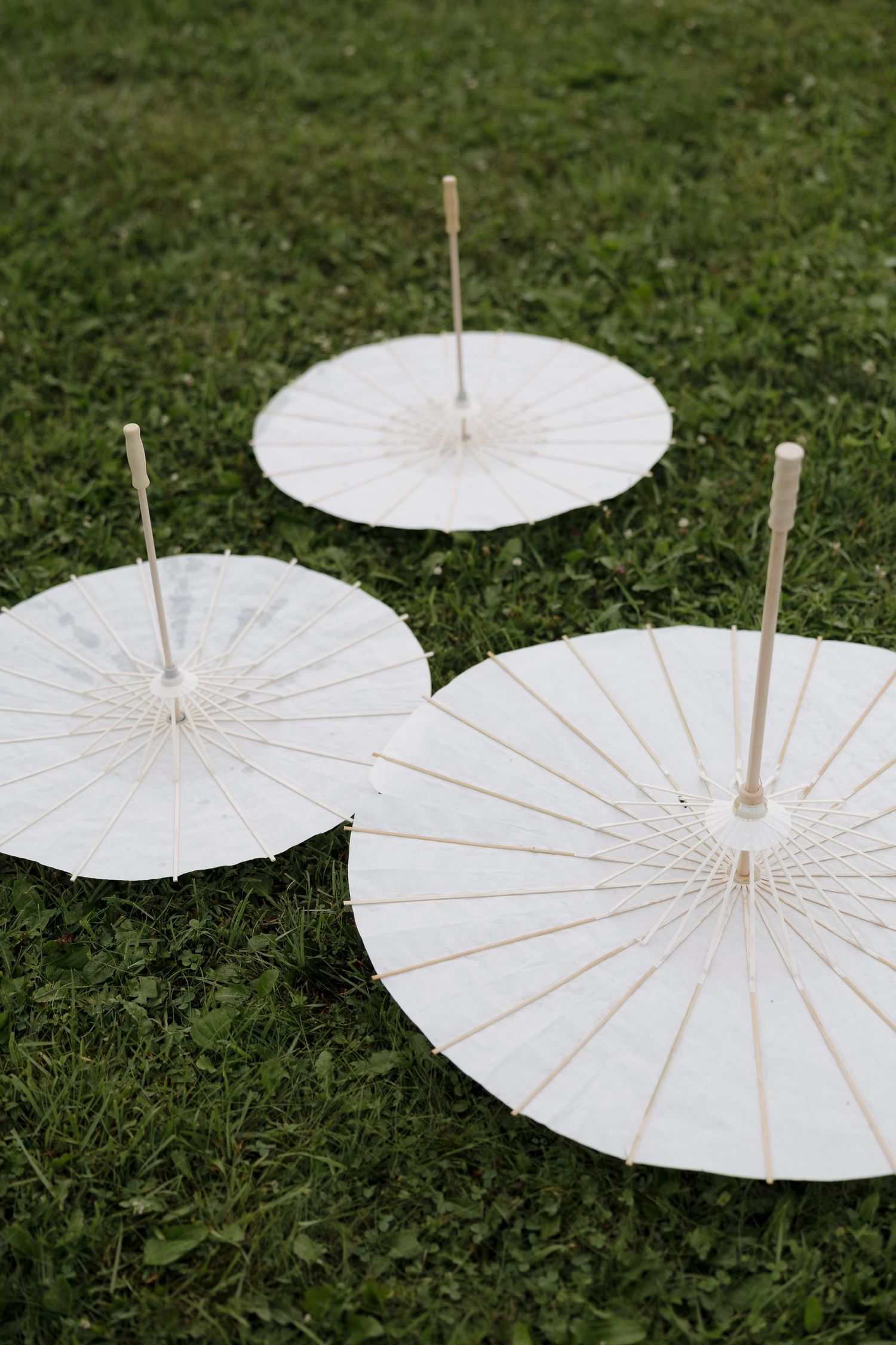 Three white paper parasols arranged on green grass for outdoor wedding decor.