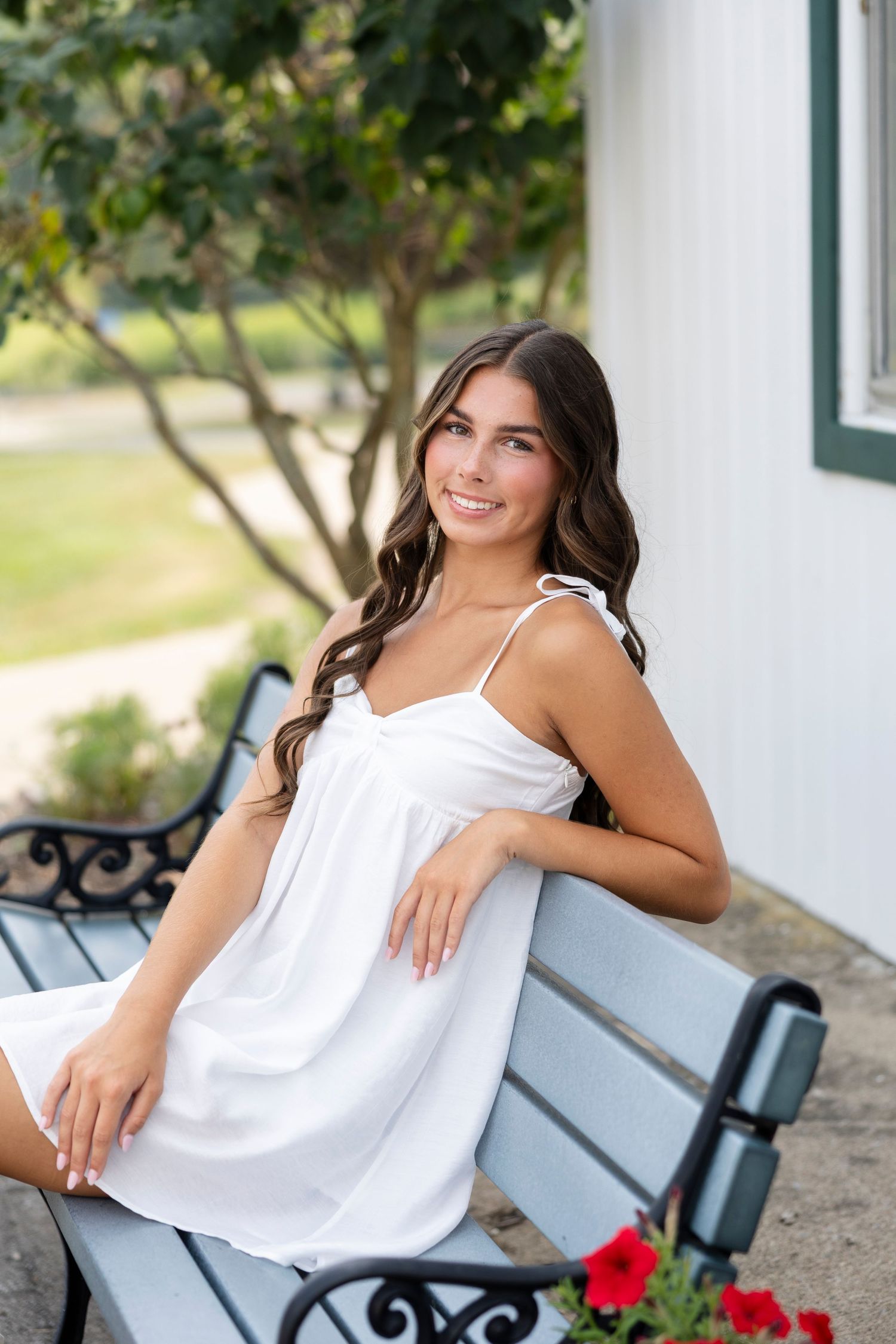 Outdoor female senior portrait session on white bench with red flower accent and stone wall background at Tinker Nature Center, Rochester NY