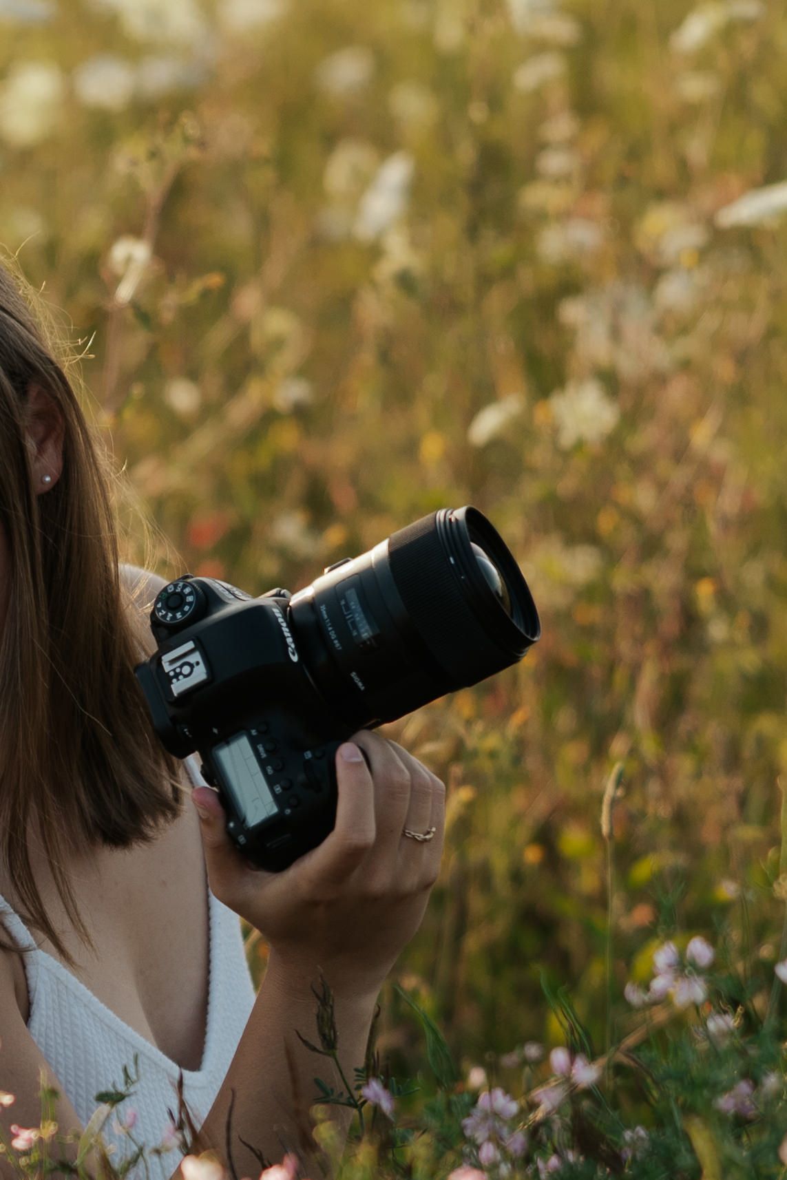 Photographer using a professional DSLR camera with telephoto lens to capture nature shots in a wildflower meadow.