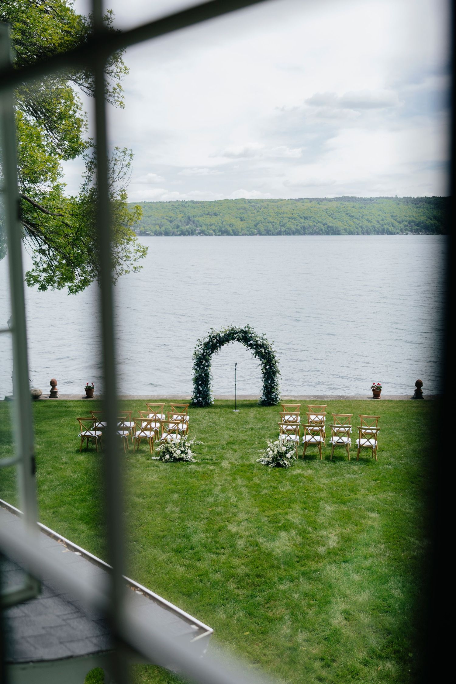 Cananandaigua Lakeside wedding ceremony setup with white chairs and floral arch overlooking water.