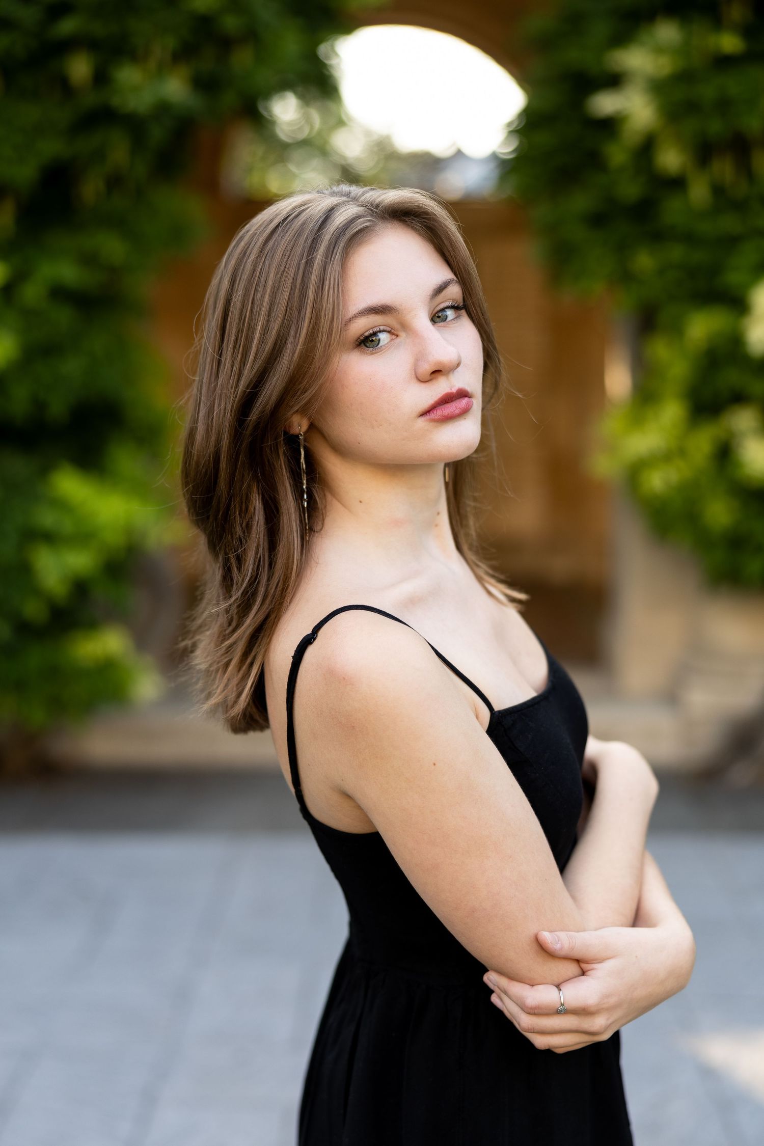 Person in black dress poses elegantly against blurred outdoor background of George Eastman House arch in Rochester NY senior photos.