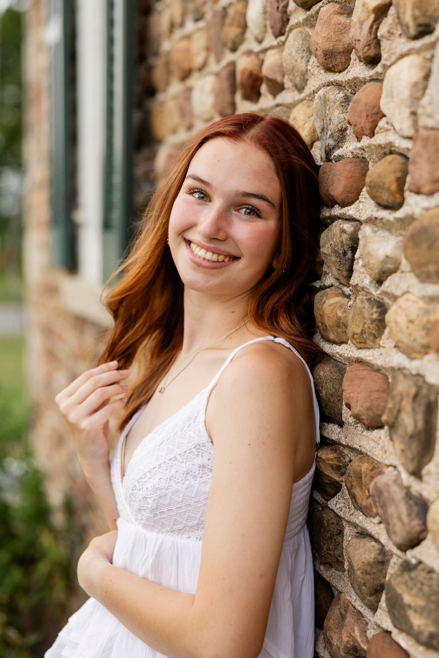 Portrait session against rustic stone wall wearing white summer dress at Tinker Nature Center for Rochester NY senior portaits.