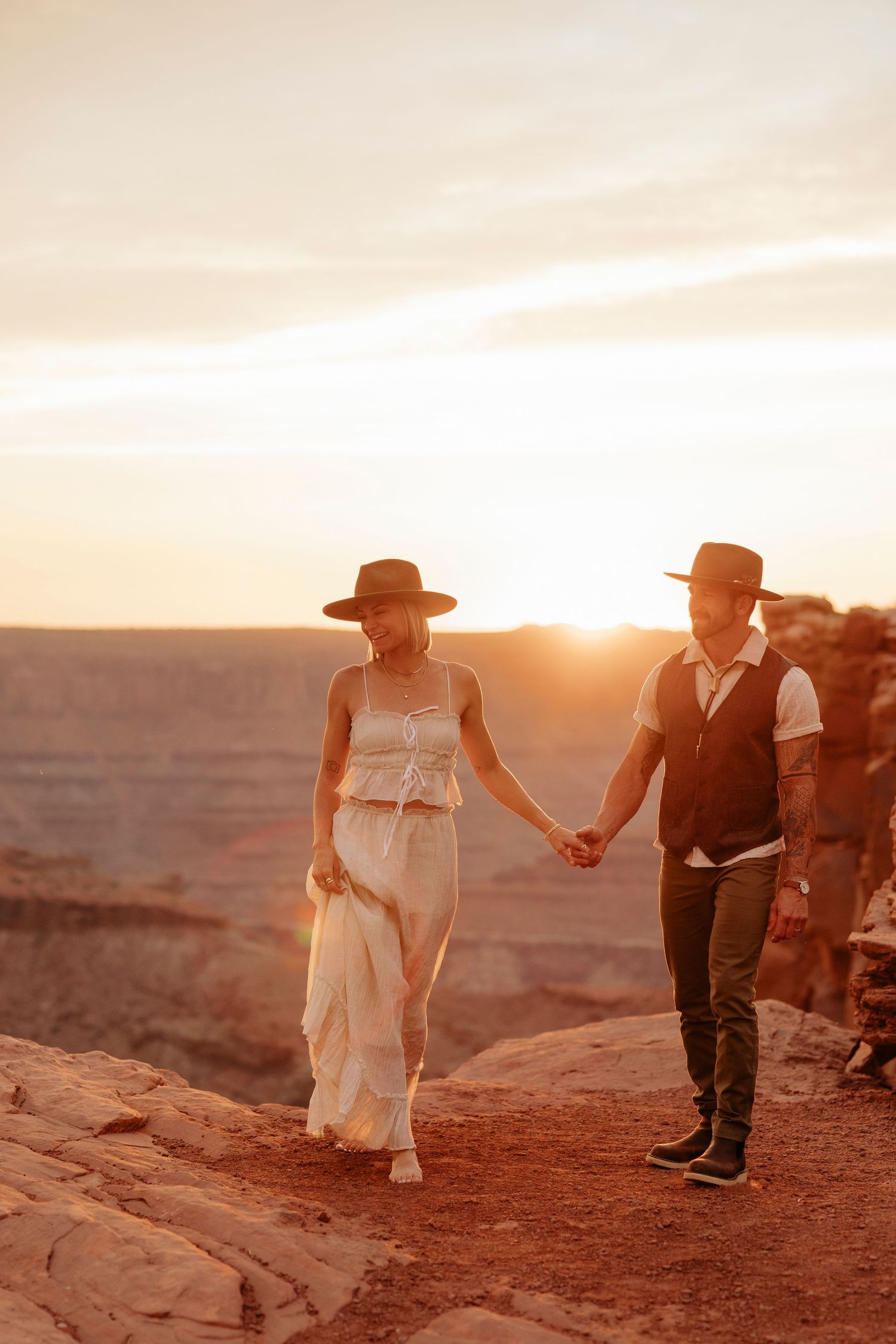 A couple walks hand in hand along red rock cliffs during golden hour at Dead Horse State Park Elopement.